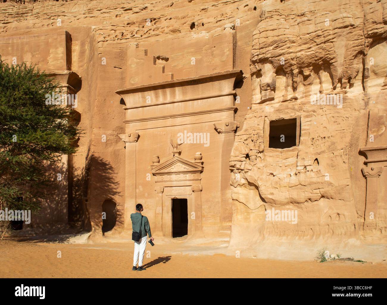 Alula, Arabie Saoudite, 4 avril 2024. Vue arrière d'un seul touriste mâle debout devant la tombe rocheuse à Hegra dans une journée ensoleillée. Banque D'Images Alula, Arabie Saoudite, 4 avril 2024. Vue arrière d'un seul touriste mâle debout devant la tombe rocheuse à Hegra dans une journée ensoleillée. Banque D'Images