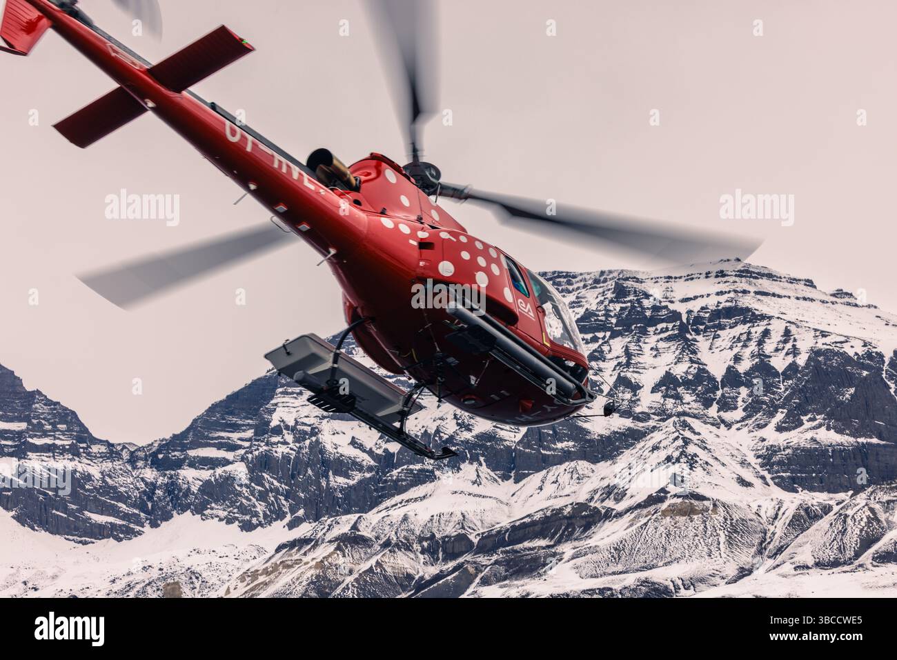 Hélicoptère rouge volant bas au-dessus du terrain glacé et des sommets déchiquetés dans l'ouest du Groenland. Banque D'Images