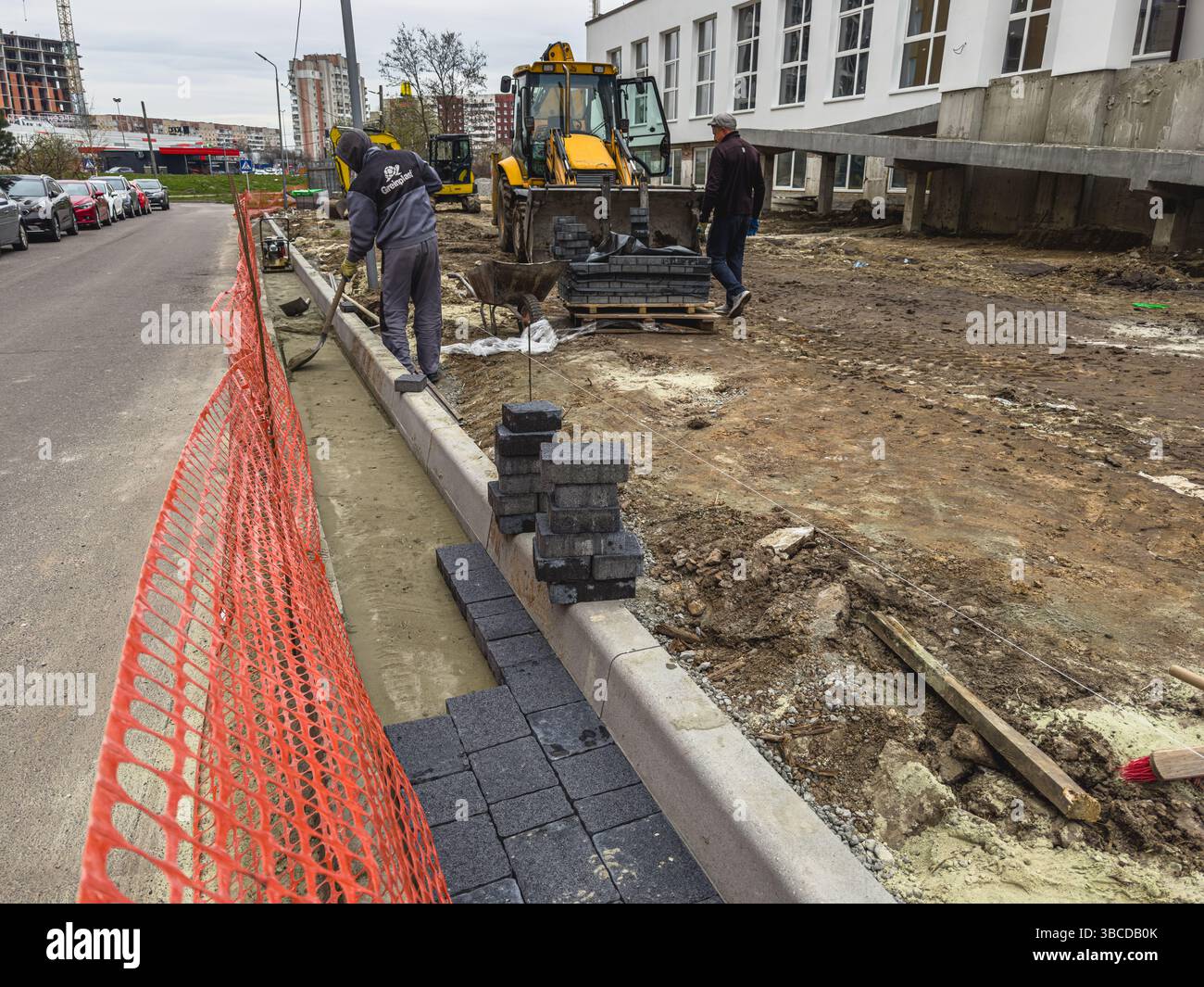 Lviv Ukraine 04.15.25 travailleurs de la construction sont occupés à poser de lourds blocs de chaussée le long d'une rue en rénovation, avec des équipements et des matériaux à proximité, Banque D'Images