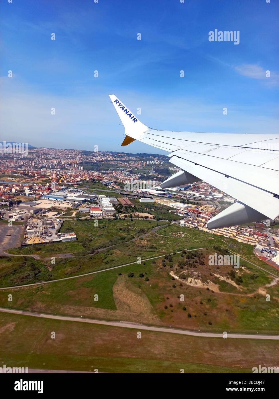 Espagne. 12 avril 2023 Escadre d'un avion de Ryanair en descente montrant un paysage urbain tentaculaire et une campagne ouverte sous un ciel bleu clair Banque D'Images