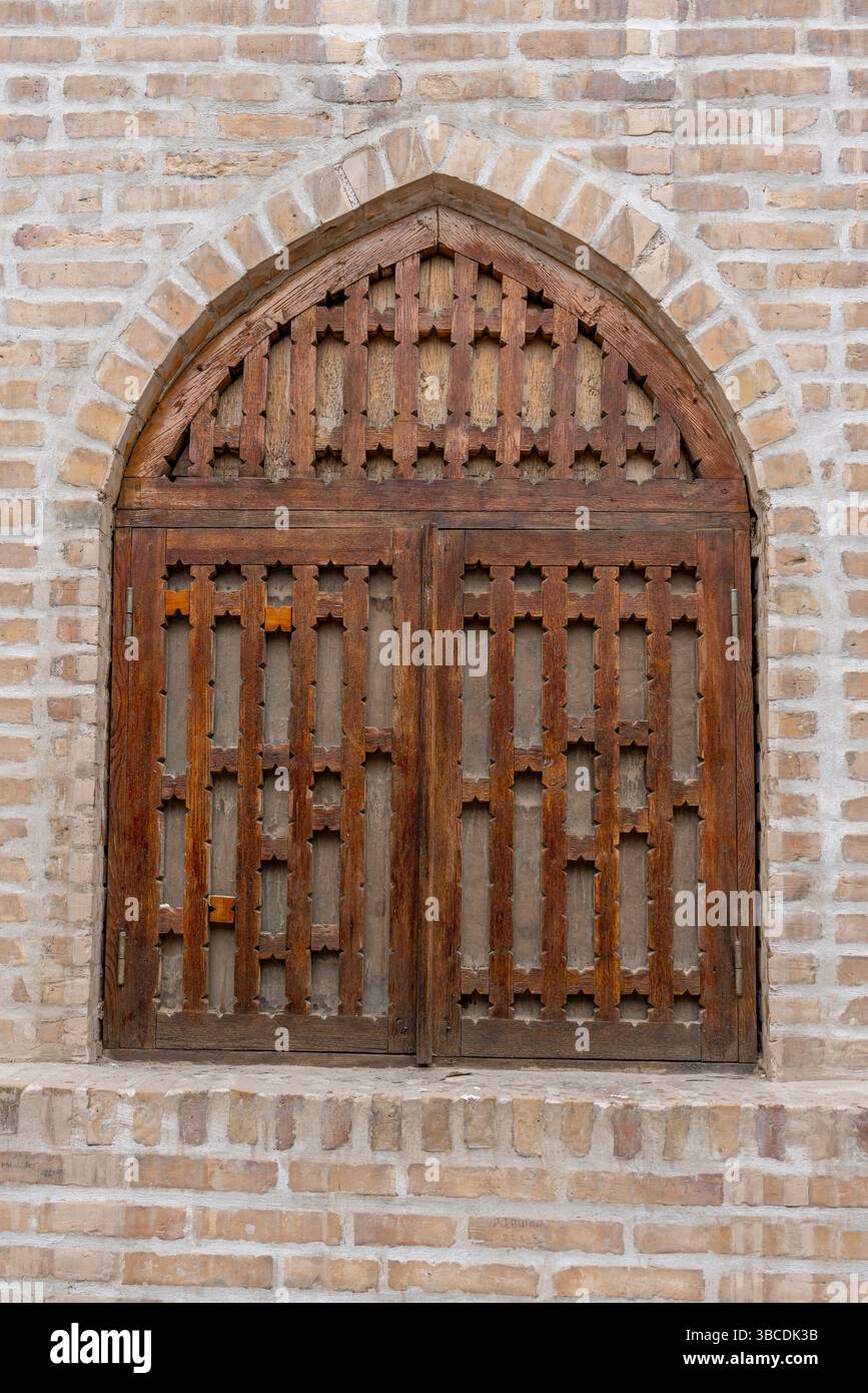 Une fenêtre traditionnelle en bois avec des treillis complexes est située dans un mur de briques à Boukhara, en Ouzbékistan, montrant l'artisanat local. Banque D'Images