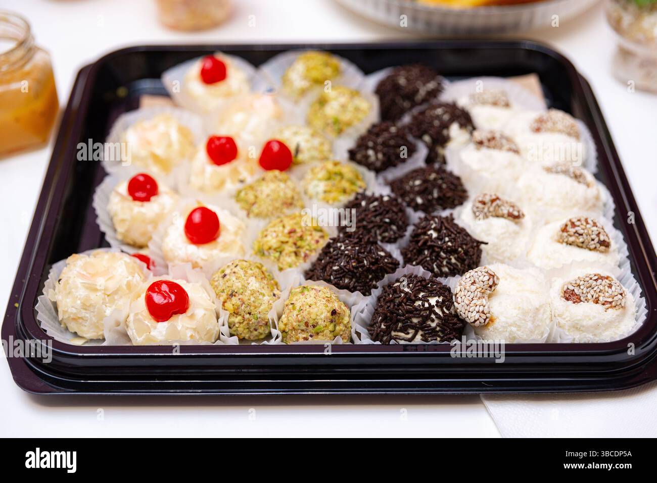 Élégant plateau de boules de dessert assorties enrobées de pistaches, de saupoudrées de chocolat, de noix de coco, de cerises et de sésame - idéal pour les événements ou les cadeaux. Banque D'Images