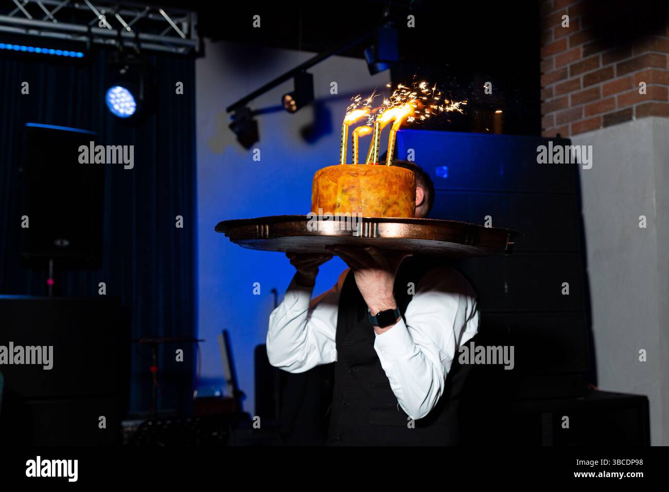 Waiter présente un gâteau surmonté de scintillants brûlants lors d'un événement festif, capturé dans un éclairage dramatique pour un moment spécial. Banque D'Images
