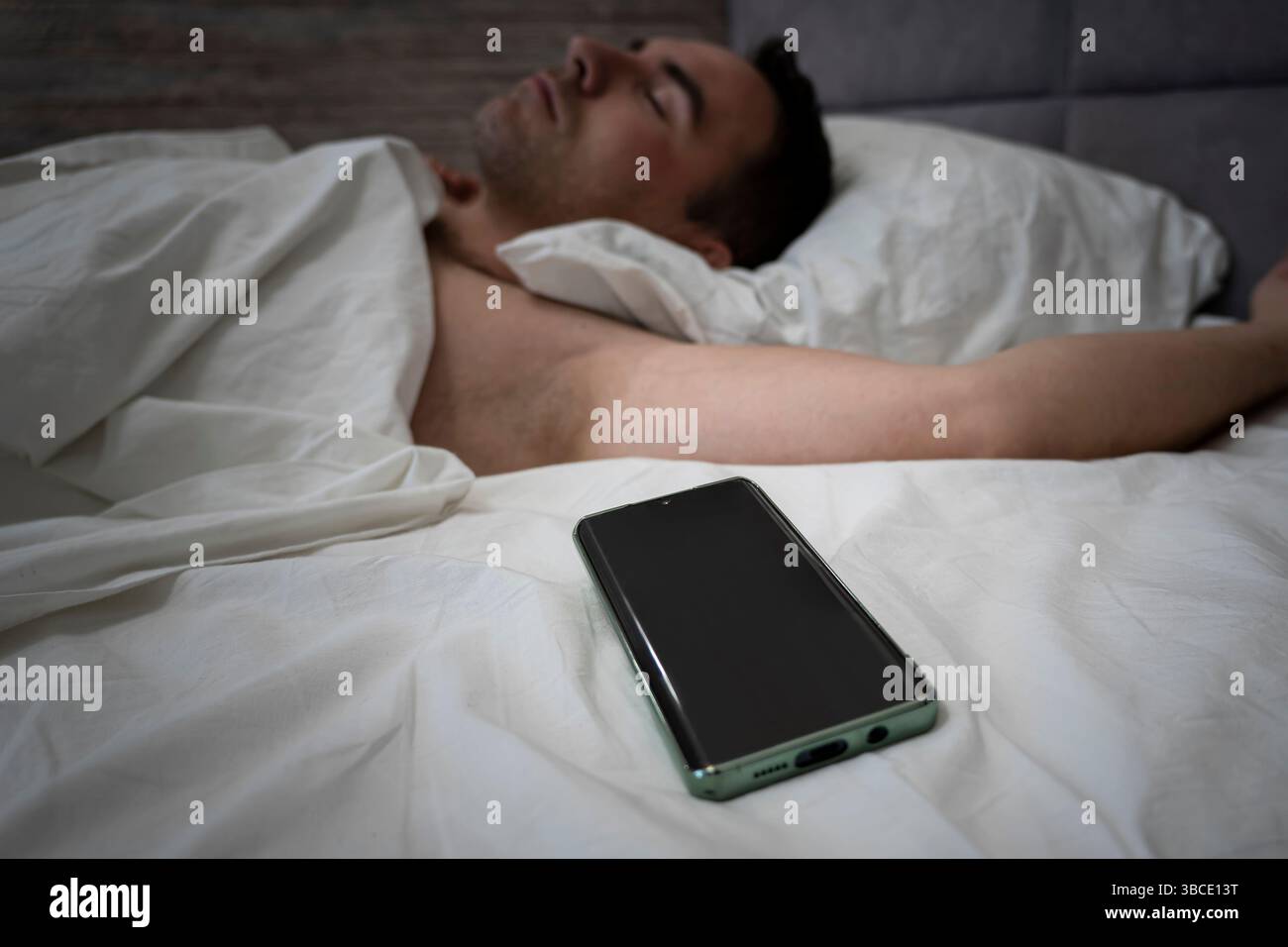 Jeune homme sifflant sur le lit. Utilisateur de smartphone tenant son téléphone portable pendant qu'il dort. Concept Mobile Addiction. un écran de smartphone vierge pour le texte et le design. Banque D'Images