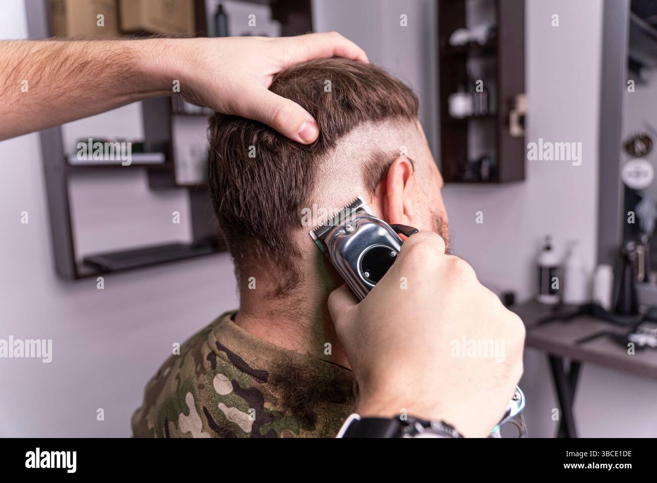 Un jeune homme dans un uniforme militaire se prépare à la tête chauve pour le service militaire. Un homme avec une barbe obtient une coupe de cheveux dans un salon de coiffure. Banque D'Images