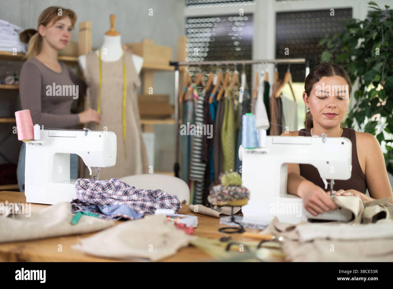 Tailleur femme travaillant sur une machine à coudre avec un assistant en arrière-plan Banque D'Images
