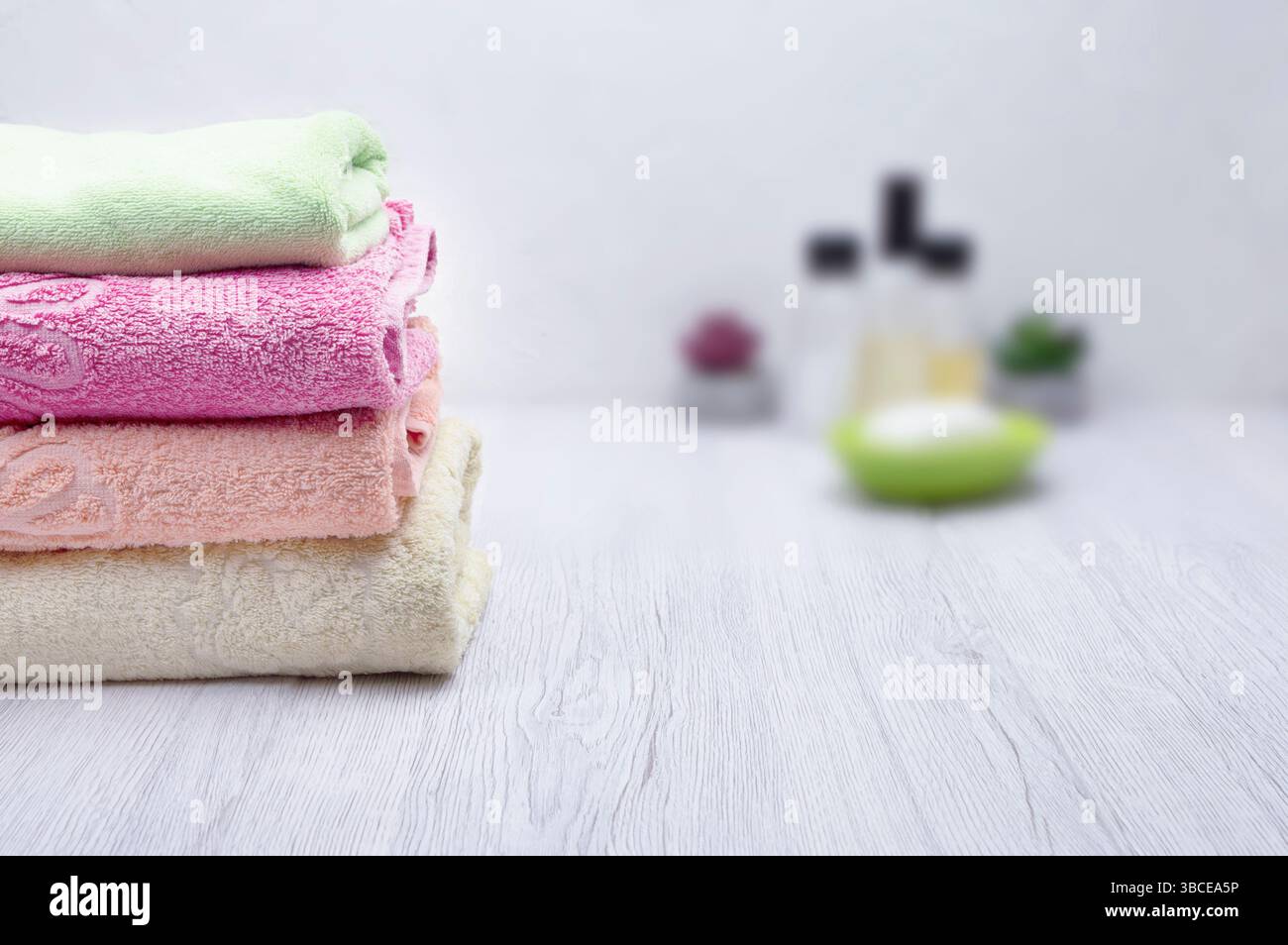 Une pile de serviettes roses dans une salle de bain, accompagnées de shampooing, revitalisant et savon, offrant un espace pour le contenu promotionnel. Banque D'Images