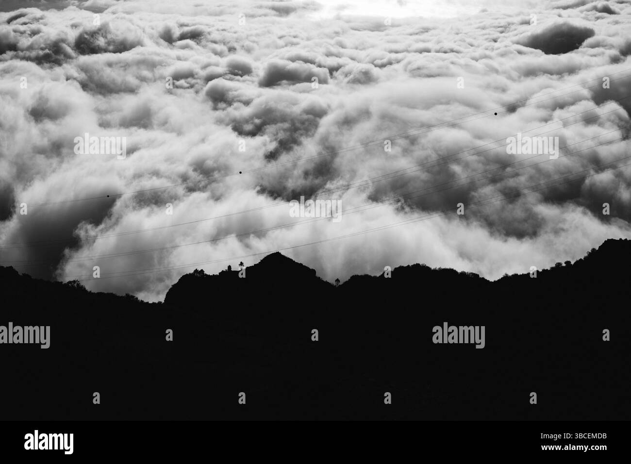 Silhouette montagneuse noire et blanche spectaculaire contre une mer de nuages avec des lignes électriques Banque D'Images