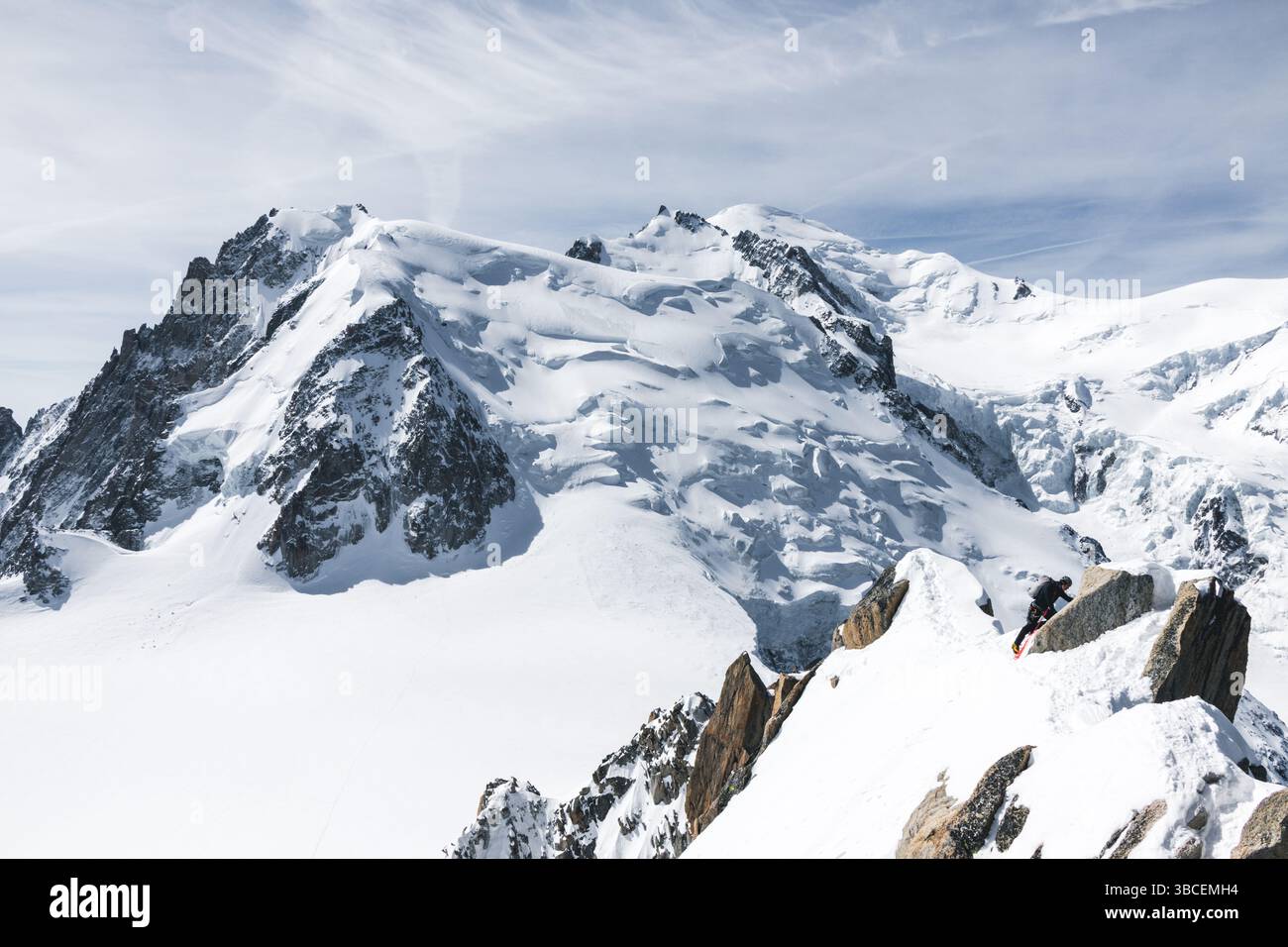 Un alpiniste avec corde, piolet et crampons sur une crête rocheuse, avec vue sur le massif du Mont Blanc en arrière-plan. Prise de l'aiguille du midi. Banque D'Images
