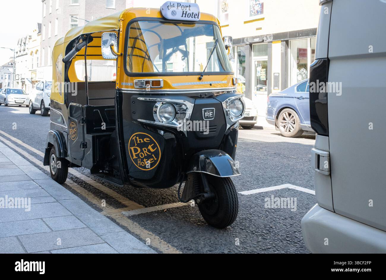 Portrush, Irlande du Nord - 19 mai 2025 : 3 roues Bajaj RE auto rickshaw tuk-tuk en noir et jaune, Port Hotel logo, garé, nouveau transport Banque D'Images