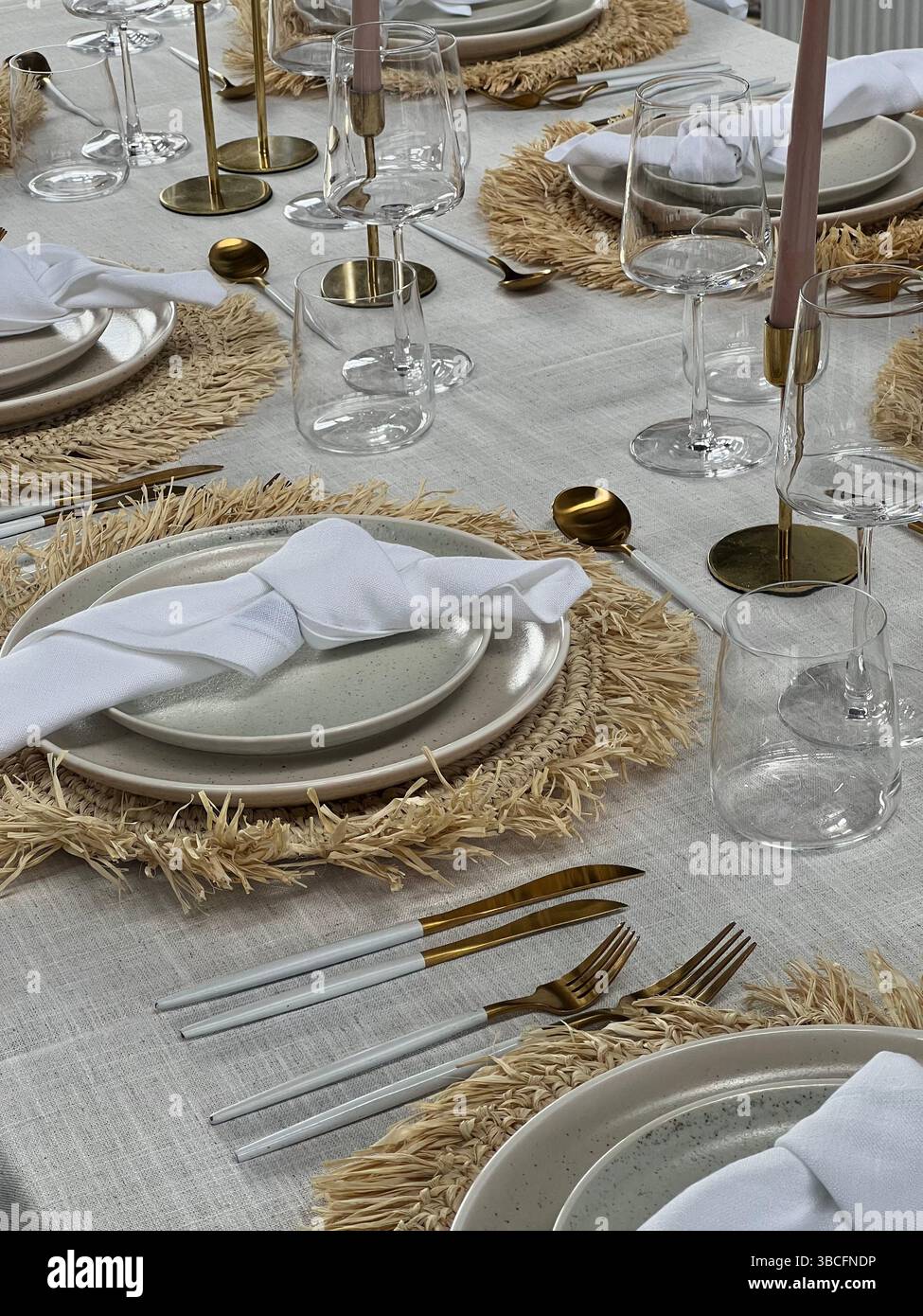 Table élégante aux tons neutres, décorée de sets de table tissés, de couverts dorés, de serviettes en lin blanc et de bougies roses. Banque D'Images