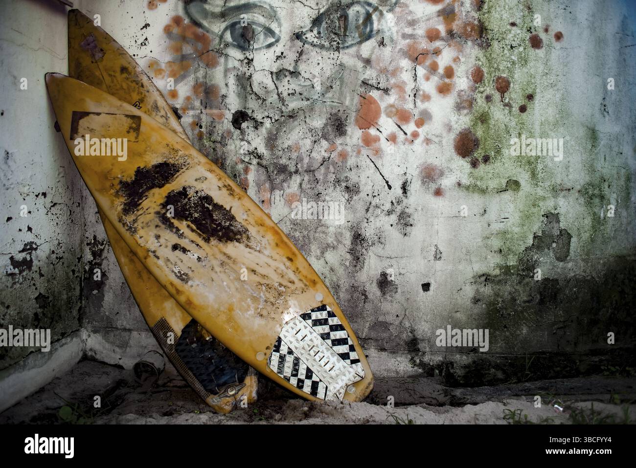 Deux vieilles planches de surf sont empilées contre un mur moisi avec des graffitis délavés et mauvais sur le mur Banque D'Images