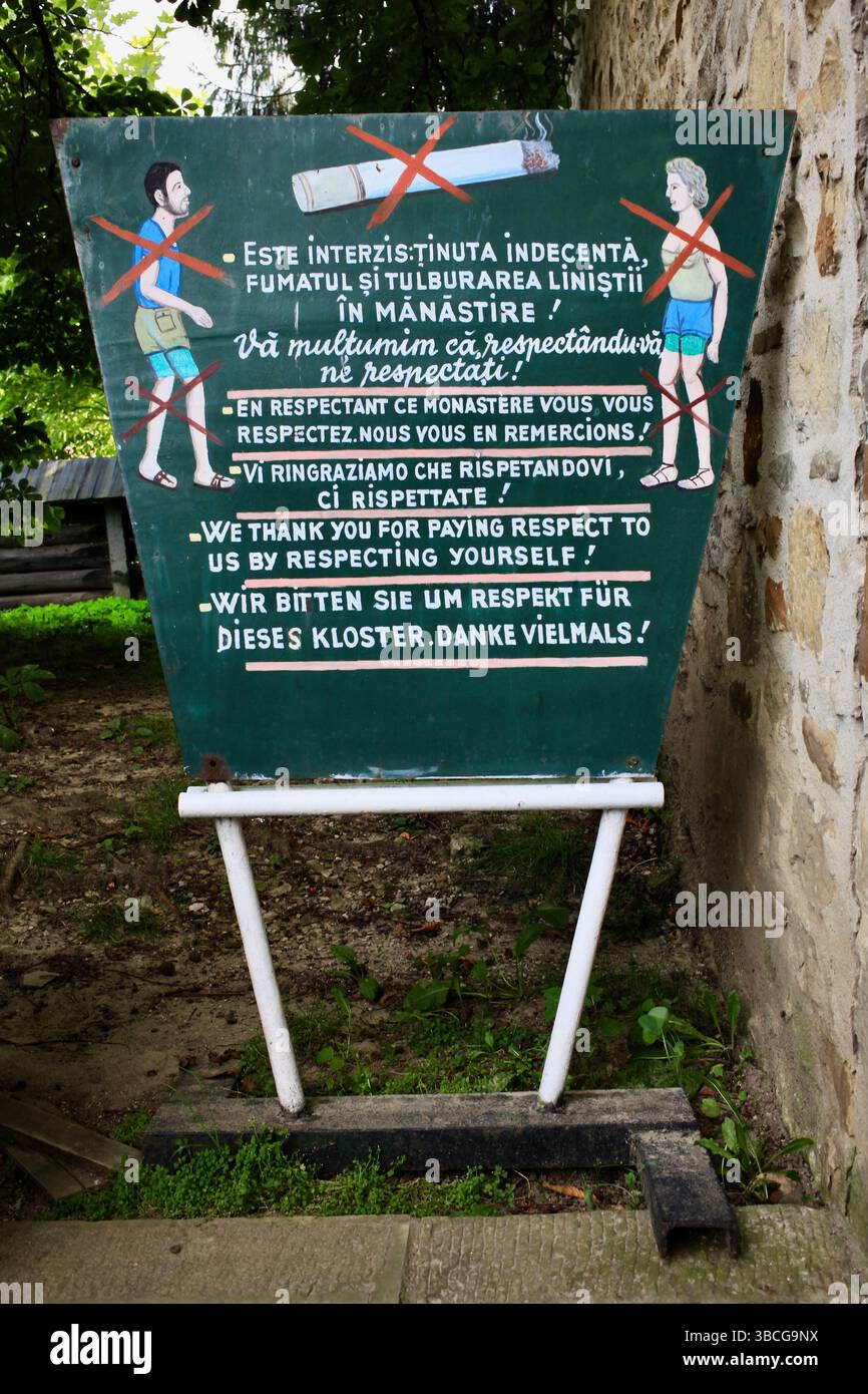 Panneau multilingue au monastère de Voroneț demandant un habillage modeste et le silence, reflétant les pressions du tourisme de masse sur les sites sacrés. Banque D'Images