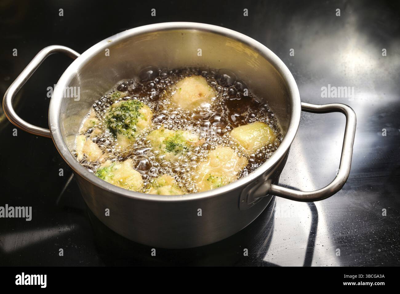 Le chou-fleur pané de bière et le brocoli sont frits dans une casserole avec de l'huile bouillante chaude sur une cuisinière noire, en cuisinant une collation végétalienne savoureuse avec des légumes Banque D'Images