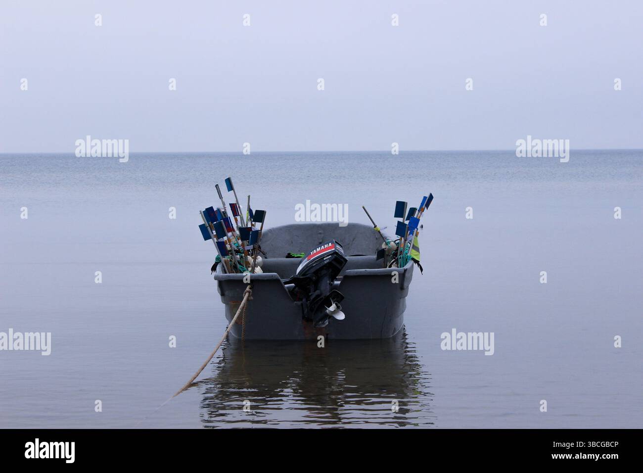 Un petit bateau de pêche gris équipé de drapeaux de signalisation colorés, ancré dans les eaux calmes d'une mer tranquille. Banque D'Images
