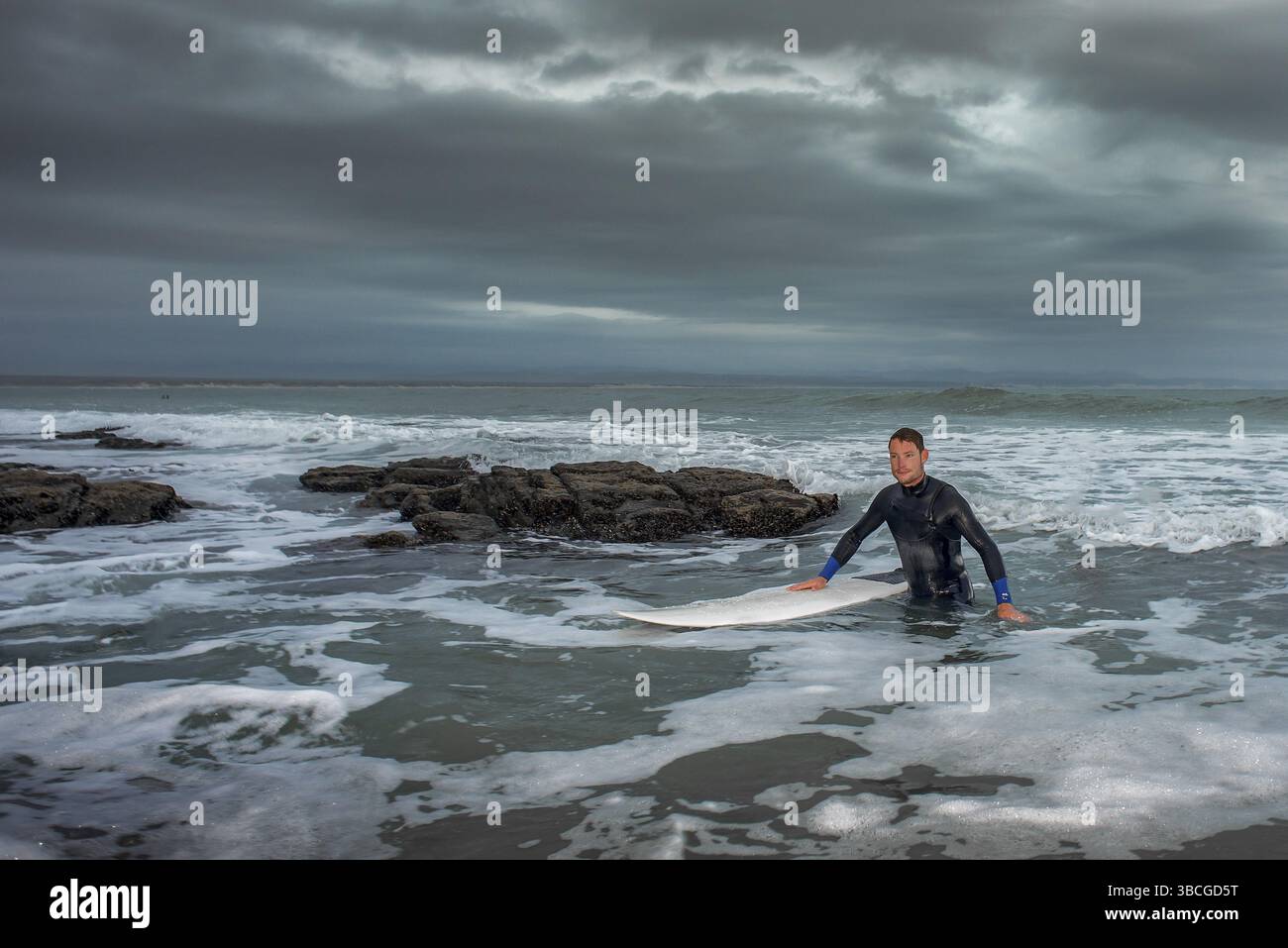 Un surfeur revient de l’océan avec sa planche de surf entre les rochers après une séance de surf Banque D'Images