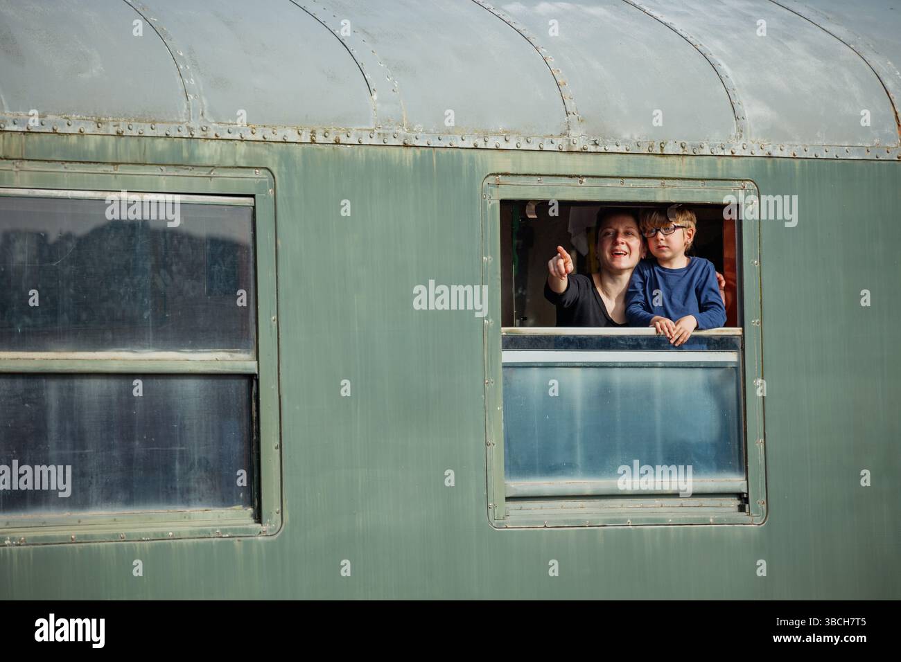 Maman avec l'enfant se penche par la fenêtre verte de calèche souriant aux champs Banque D'Images