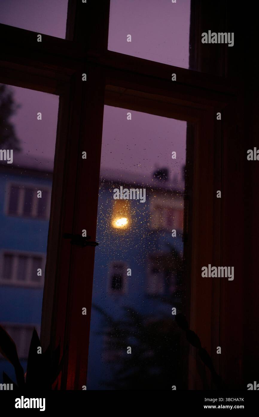 Fenêtre mouchetée avec vue sur un bâtiment bleu au crépuscule. Banque D'Images