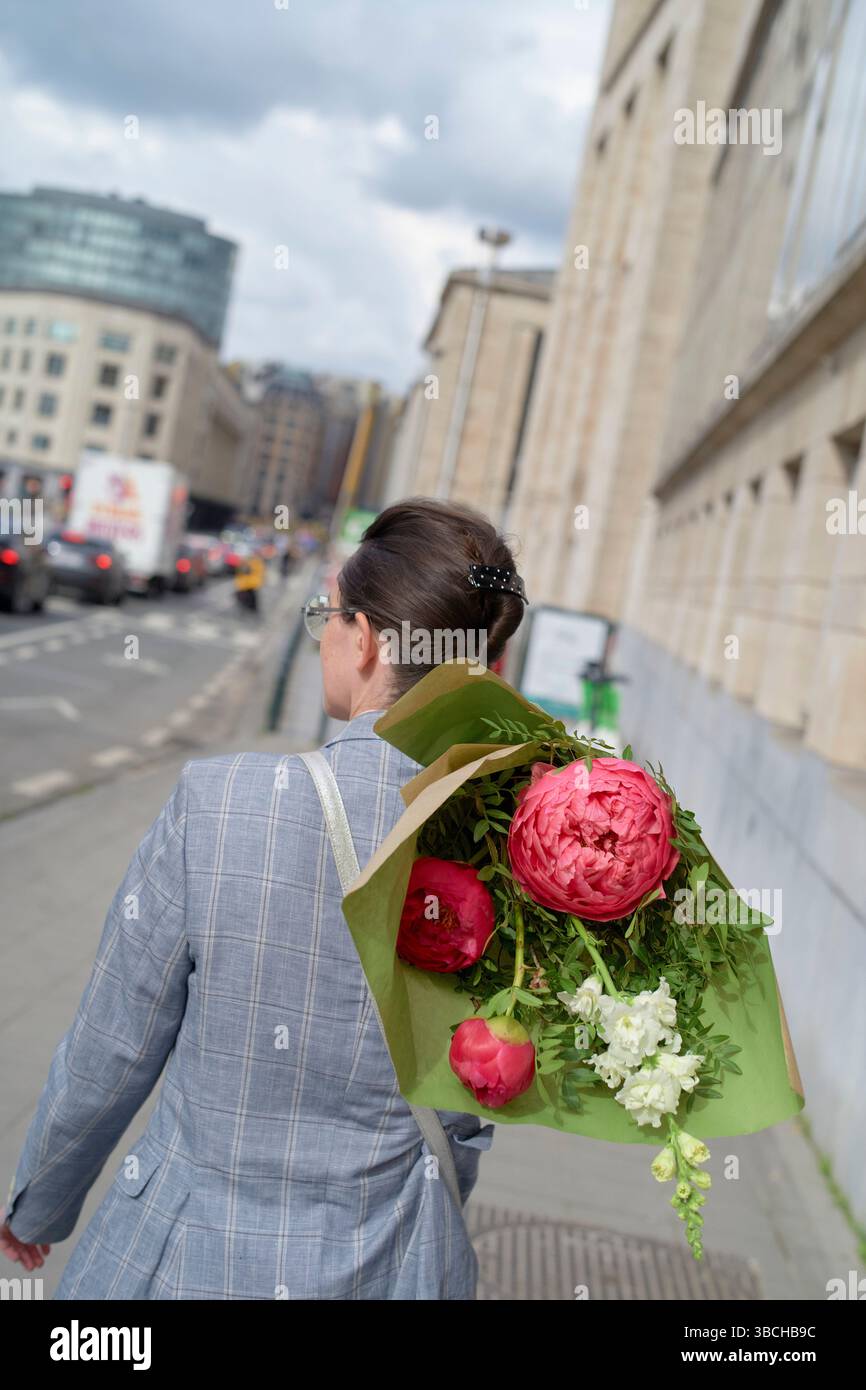 Femme marchant dans la rue de la ville avec un bouquet de fleurs roses dans un emballage vert. Banque D'Images