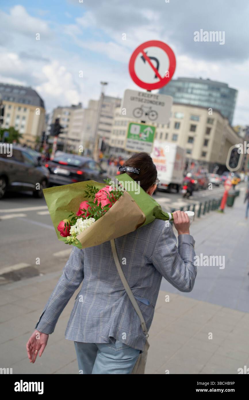 Femme marchant en ville avec bouquet de fleurs sur l'épaule. Banque D'Images