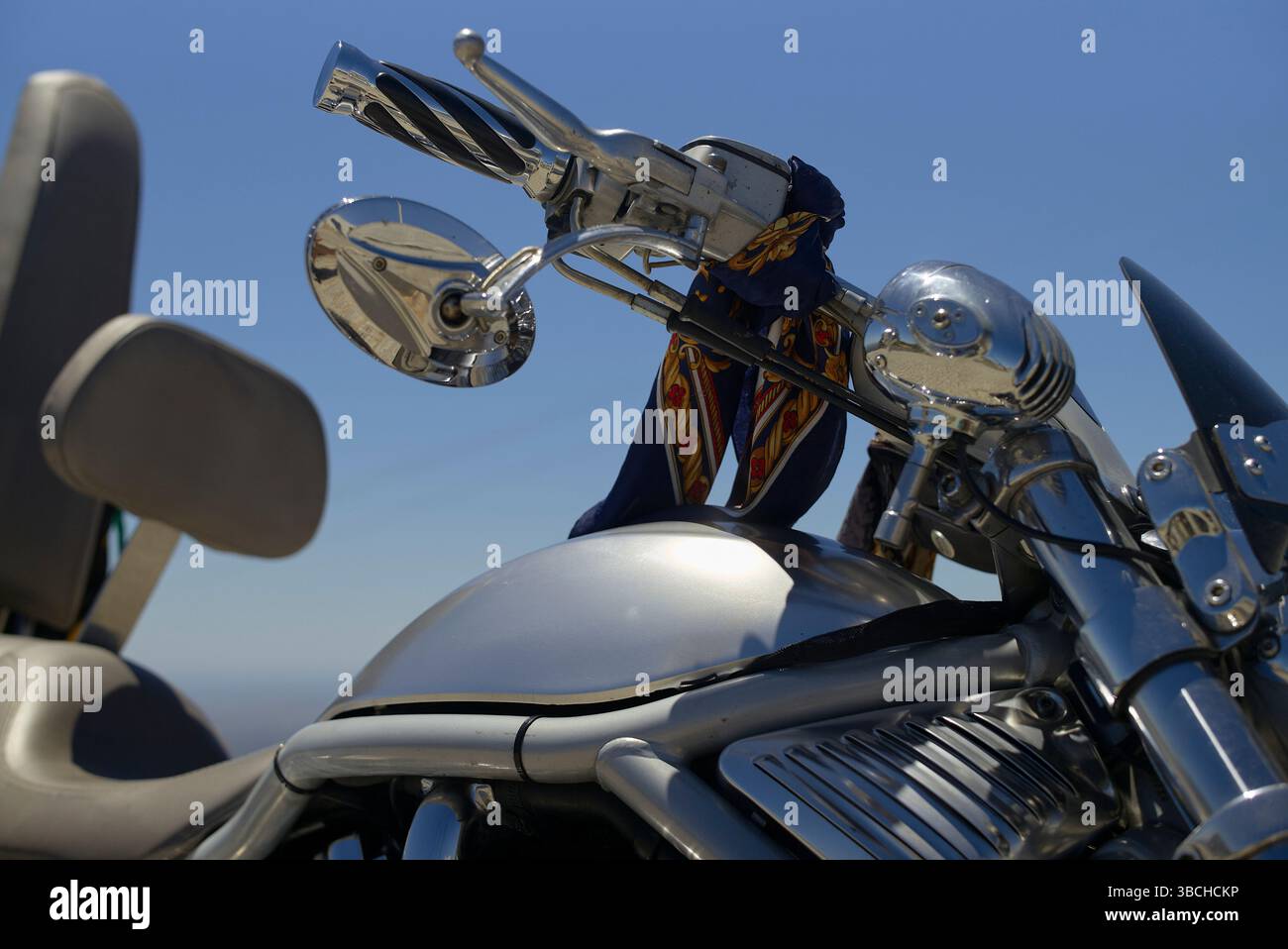 Moto chromée avec guidon orné et bandana bleu sous ciel bleu clair. Portugal Banque D'Images