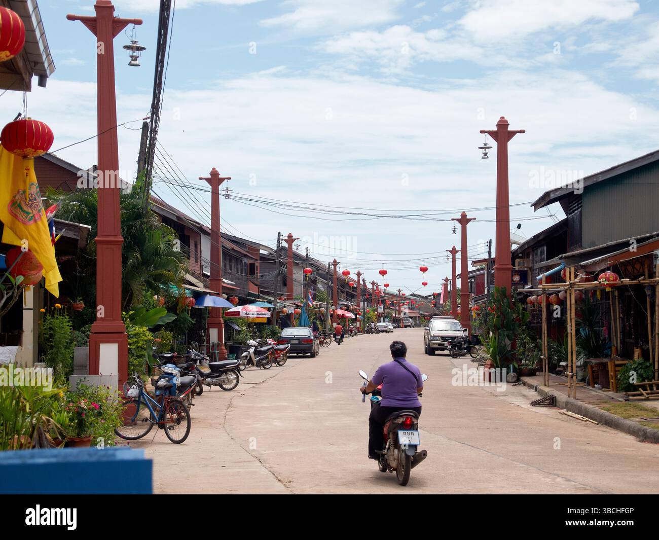 Personne sur scooter promenades à travers une rue décorée de lanternes rouges dans une ville rurale. Thaïlande Banque D'Images