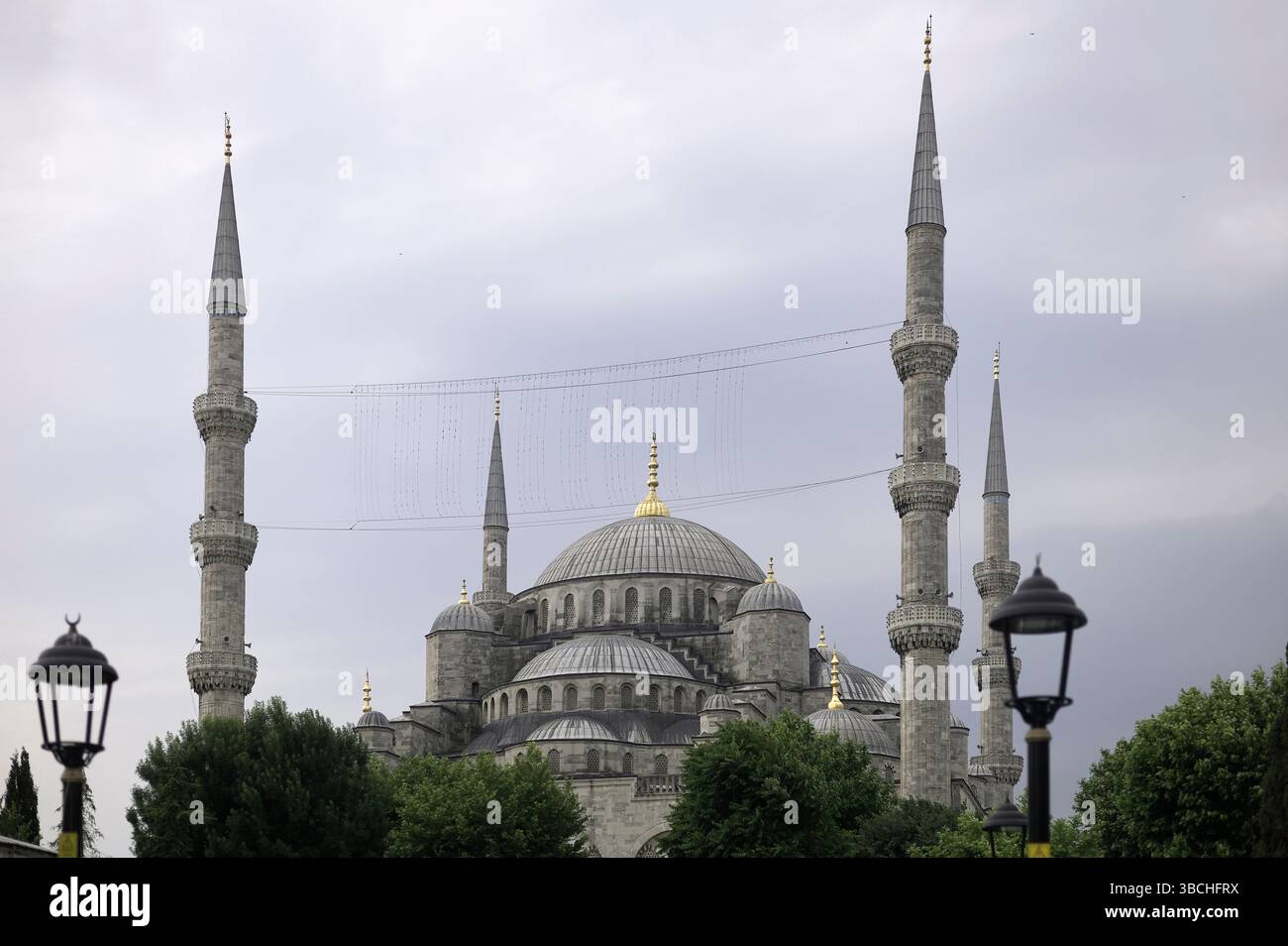 Majestueuse mosquée avec de multiples minarets contre un ciel nuageux, entourée d'arbres et de lampes. Istanbul, Turquie Banque D'Images
