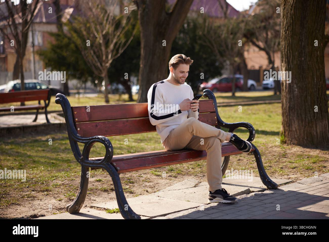 Un homme bien habillé se promène tranquillement dans un parc paisible, absorbé par son smartphone. Banque D'Images