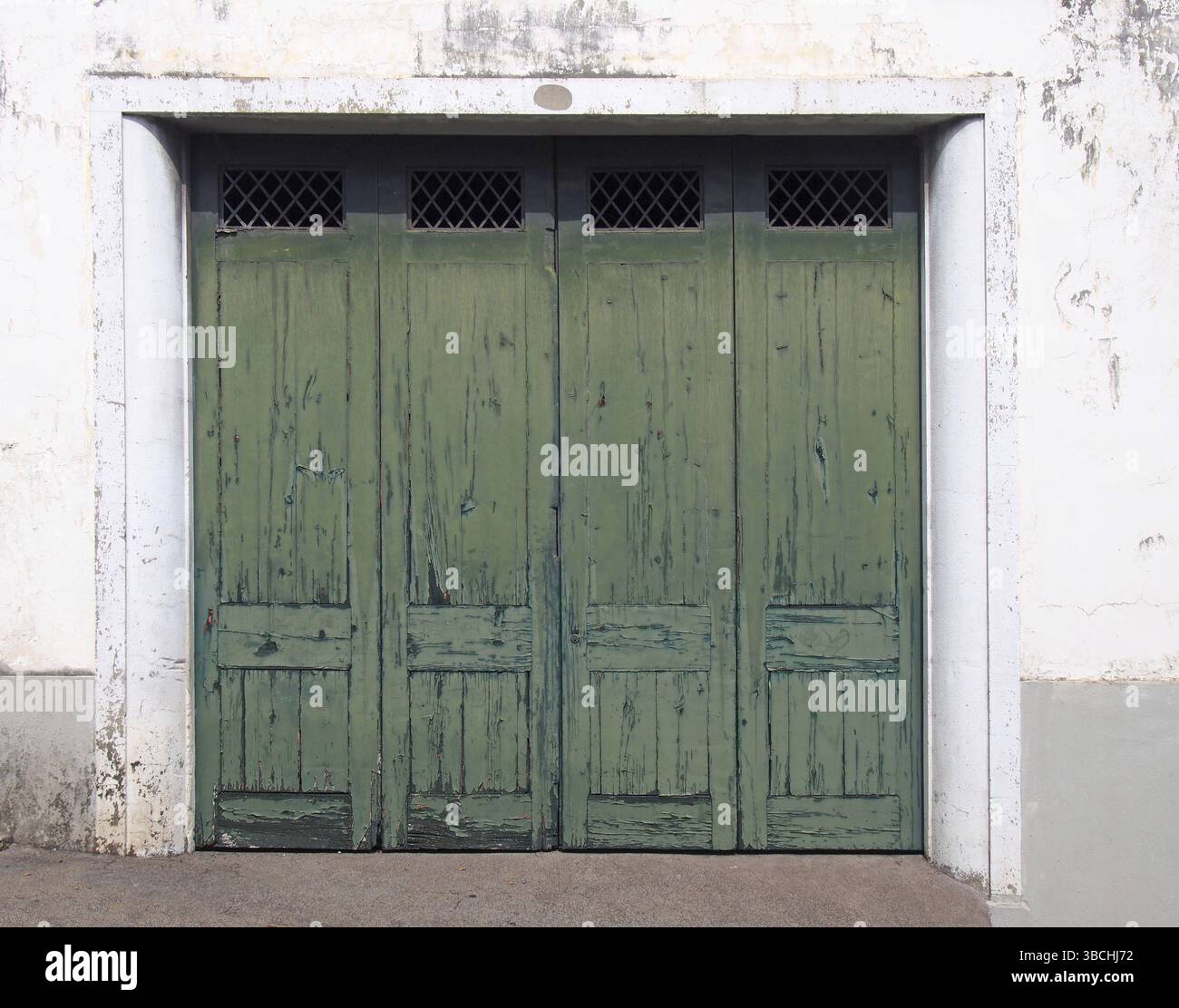 Quatre vieilles portes extérieures lambrissées en bois avec de la peinture fissurée verte décolorée dans un cadre blanc et un mur blanc vieilli Banque D'Images