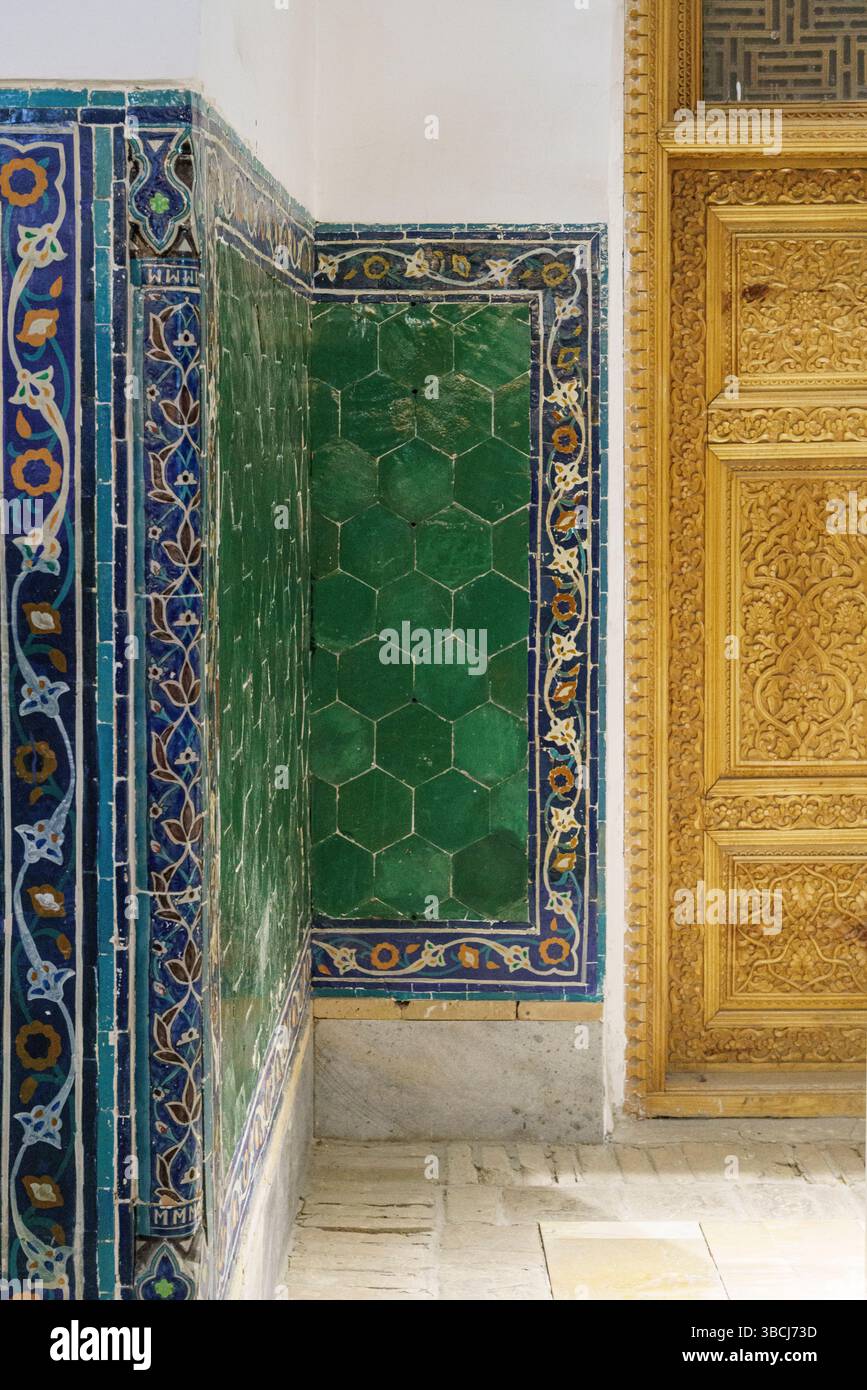 Un couloir décoré à Ulugh Beg Madrasa dans le Registan, Samarkand présente des carreaux bleus et dorés à côté d'une porte en bois sculpté au design orné. Banque D'Images