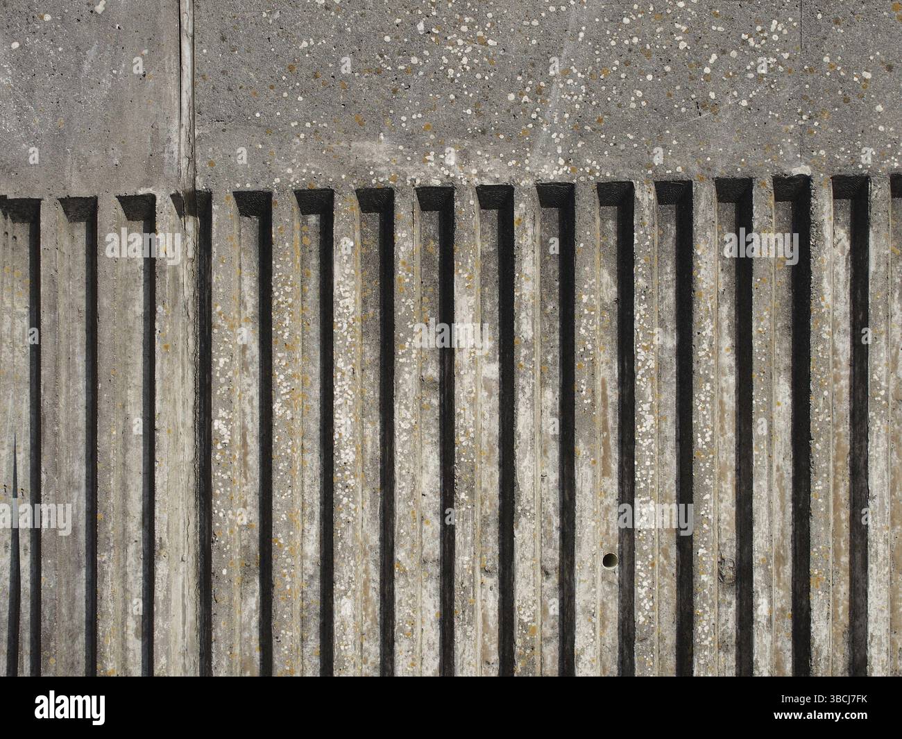 Ancien mur extérieur en béton avec motif de rayures verticales cannelées avec une texture moulée rugueuse avec ombre Banque D'Images