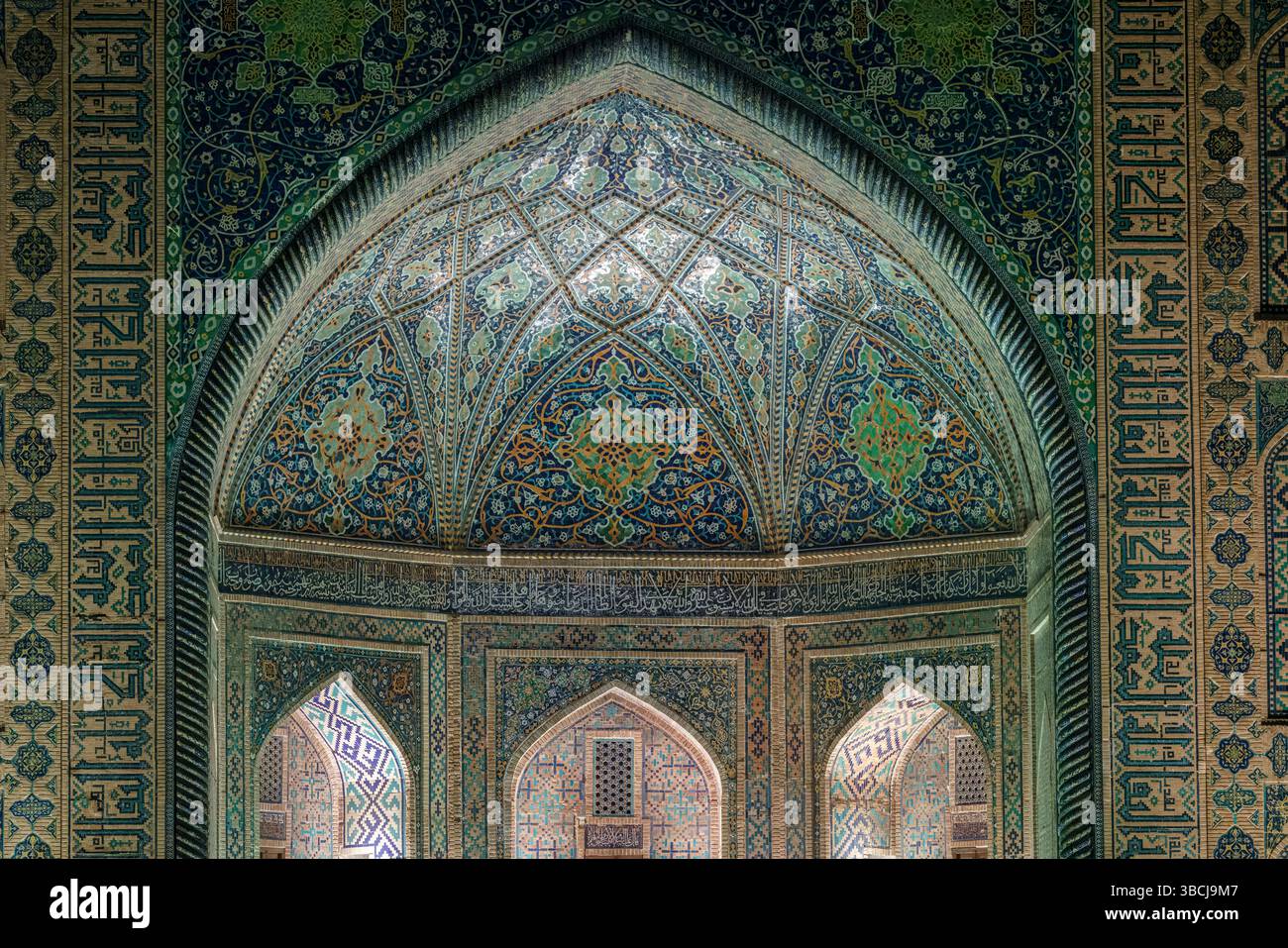 Une arche pointue remplie de délicates mosaïques bleues et dorées présente des motifs floraux et géométriques islamiques à l'intérieur de la madrasa Tilya Kori à Samarkand Banque D'Images