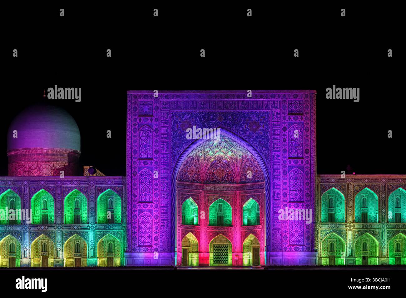 Un vif affichage de lumières violettes, vertes et jaunes transforme la Madrasa de Tilya Kori la nuit au Registan, Samarcande, Ouzbékistan, mettant en valeur ses dômes Banque D'Images