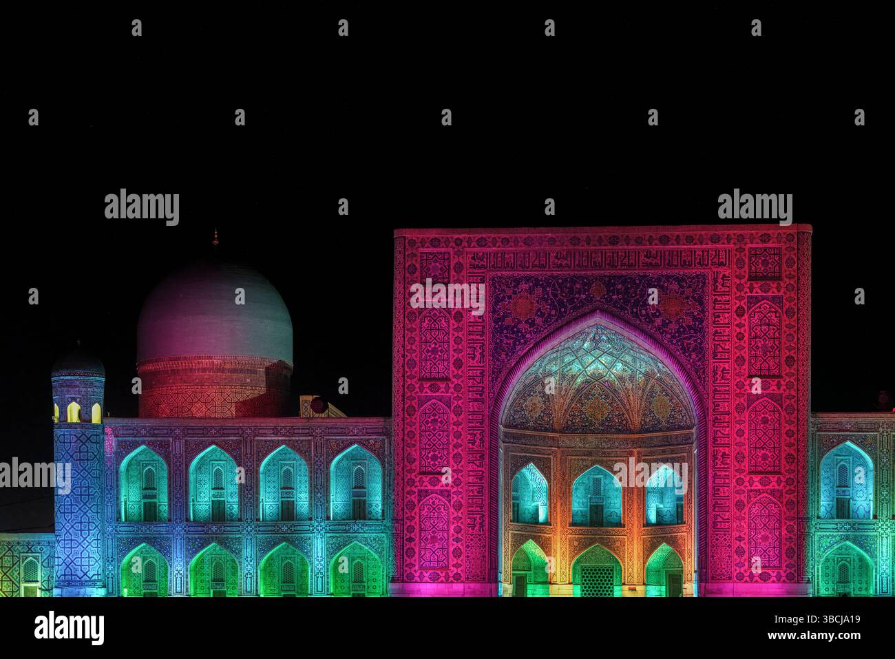 Tilya Kori Madrasa au Registan à Samarcande, Ouzbékistan, brille avec des lumières de nuit multicolores sur ses dômes, ses arches et sa façade, créant une effe de rêve Banque D'Images