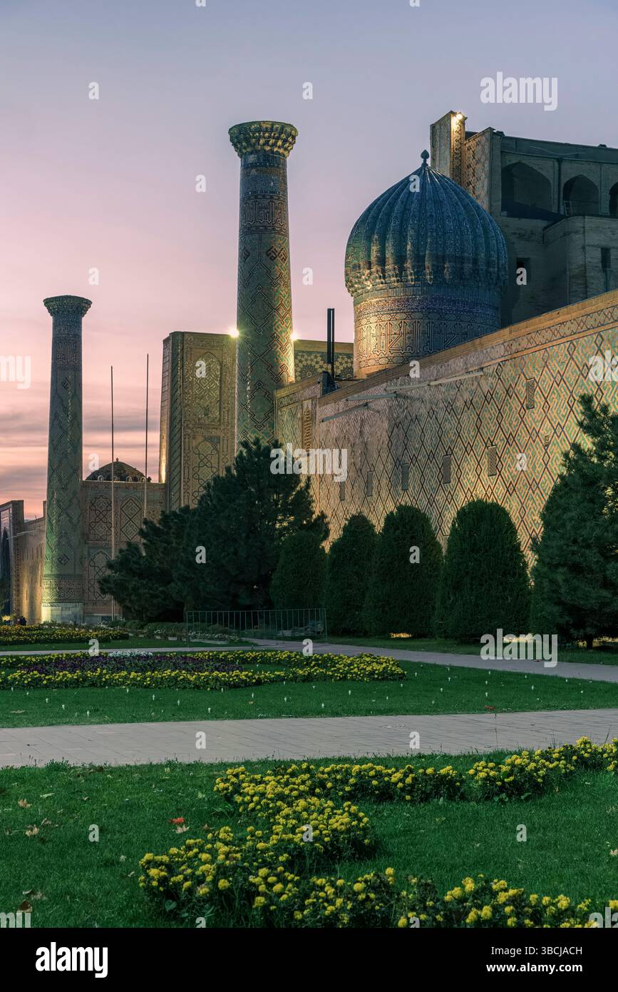 La Madrasa d'Ulugh Beg au Registan, Samarcande, Ouzbékistan, est illuminée la nuit, ses dômes et minarets brillent au-dessus des jardins bien entretenus. Banque D'Images