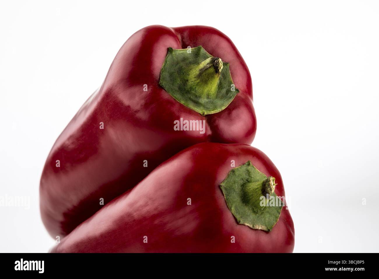 Deux paprika rouges sont couchés l'un sur l'autre, isolés sur blanc Banque D'Images