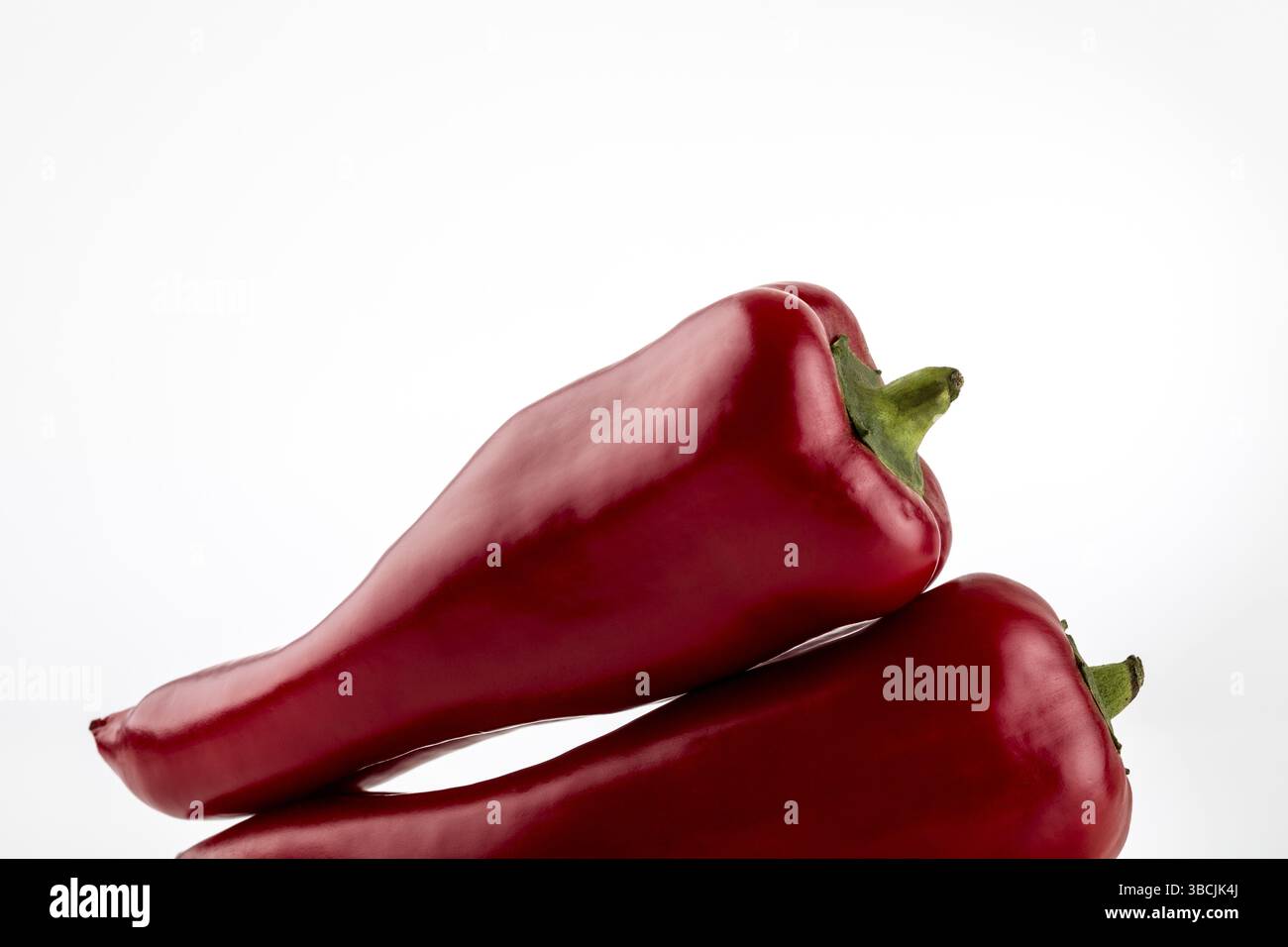 Deux paprika rouges sont couchés l'un sur l'autre, isolés sur blanc Banque D'Images
