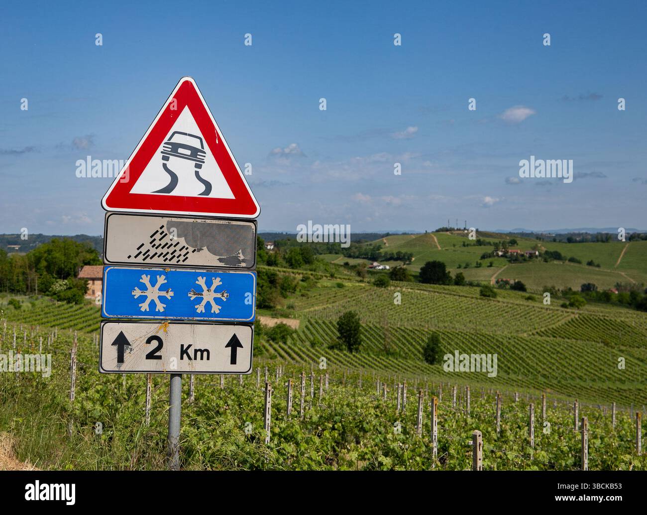 Panneau d'avertissement de la circulation Mombaruzzo Italie avec avertissement de dérapage et symbole de flocon de neige sur une route rurale avec paysage de vignoble en arrière-plan Banque D'Images