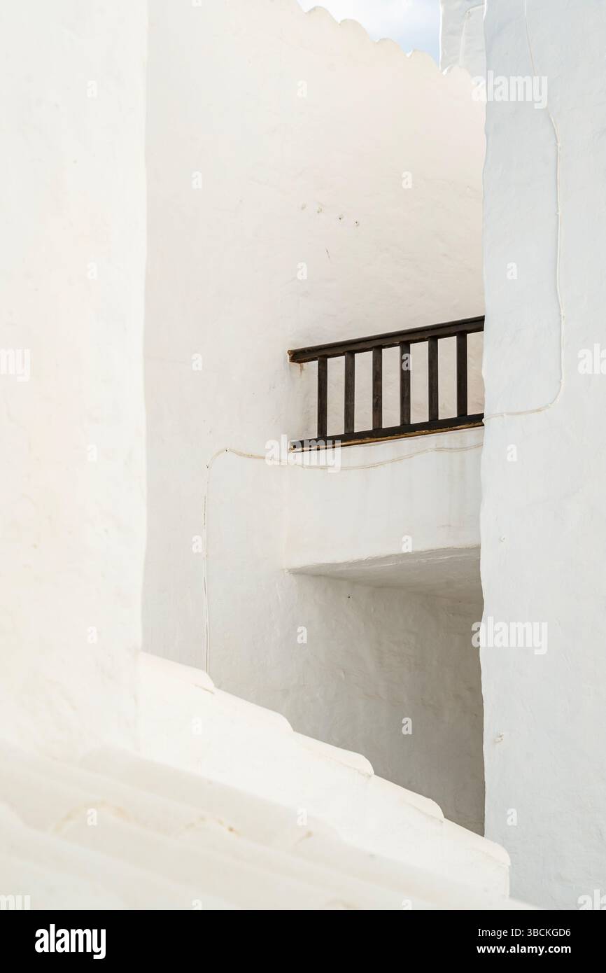 Architecture blanche minimaliste avec garde-corps sombre dans une étroite ruelle méditerranéenne. Composition abstraite, lignes épurées, lumière du soleil éclatante, murs texturés Banque D'Images