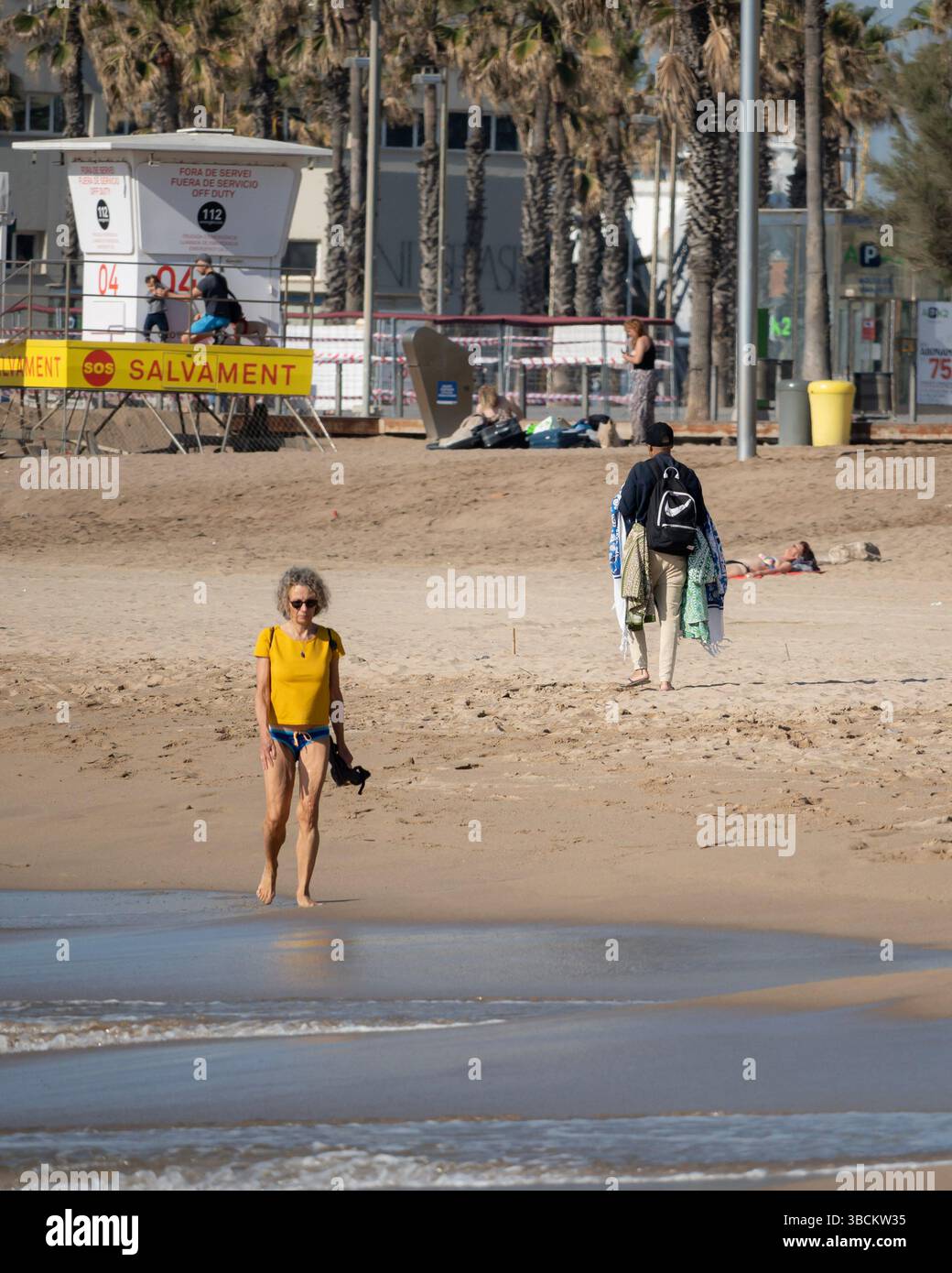 Femme senior marchant le long du rivage à la plage de Barceloneta, Barcelone, Espagne Banque D'Images