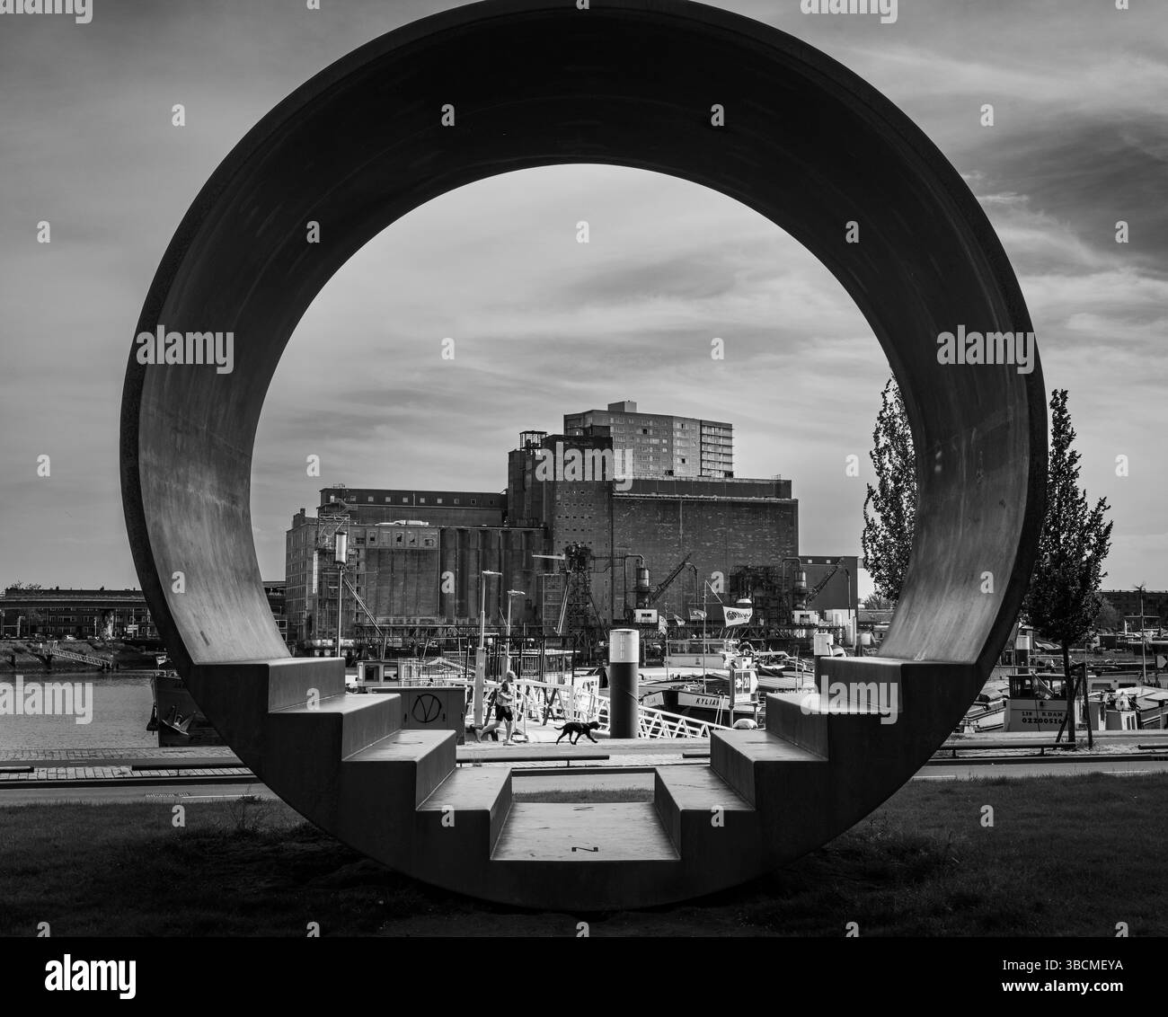 De grandes sculptures circulaires encadrent une vue sur le port industriel de Rotterdam avec une architecture moderne et historique en noir et blanc. Banque D'Images