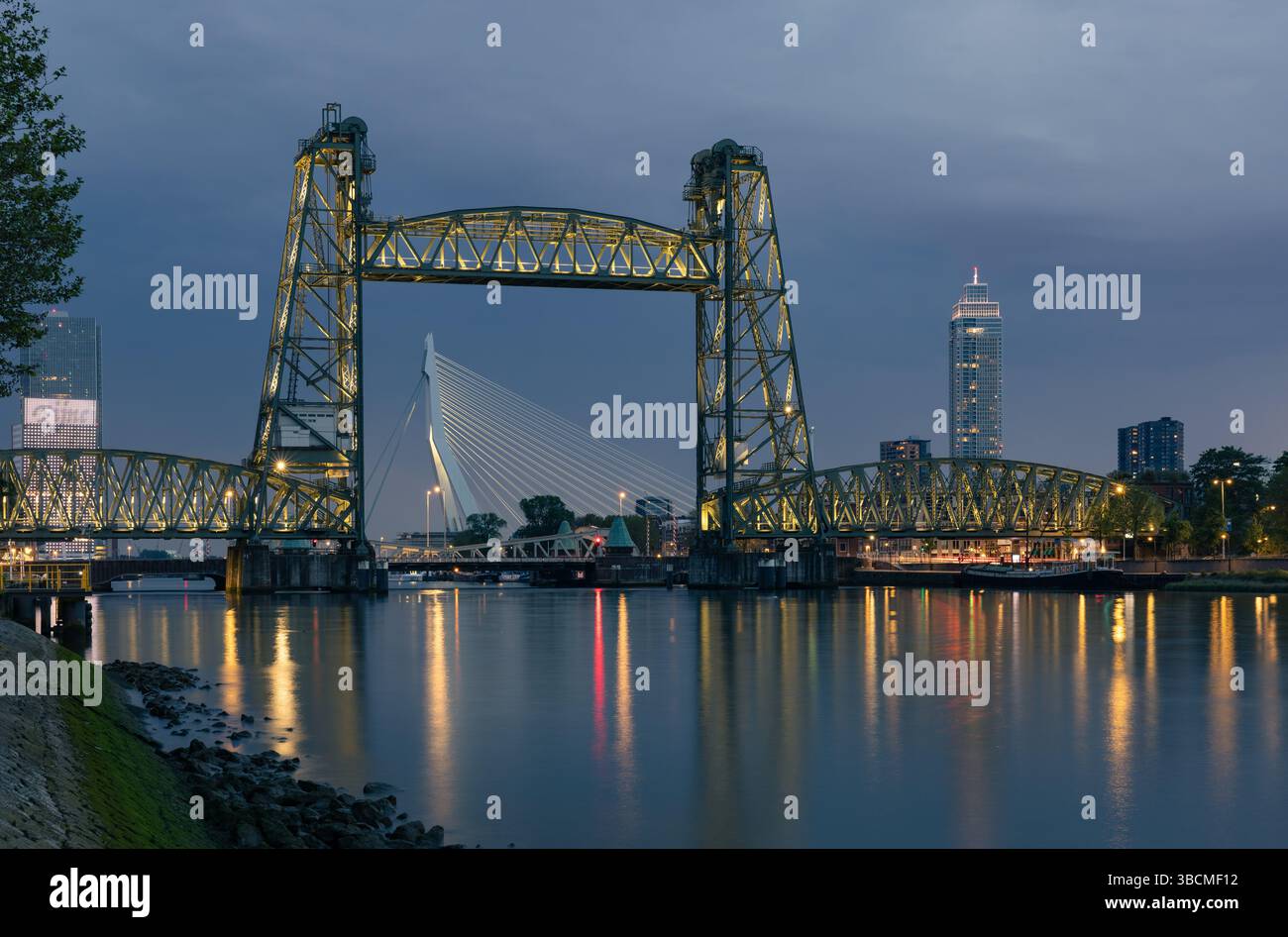 Vue nocturne des ponts Koninginnebrug et Erasmusbrug à Rotterdam, pays-Bas, avec des reflets des lumières de la ville sur la rivière calme en contrebas. Banque D'Images