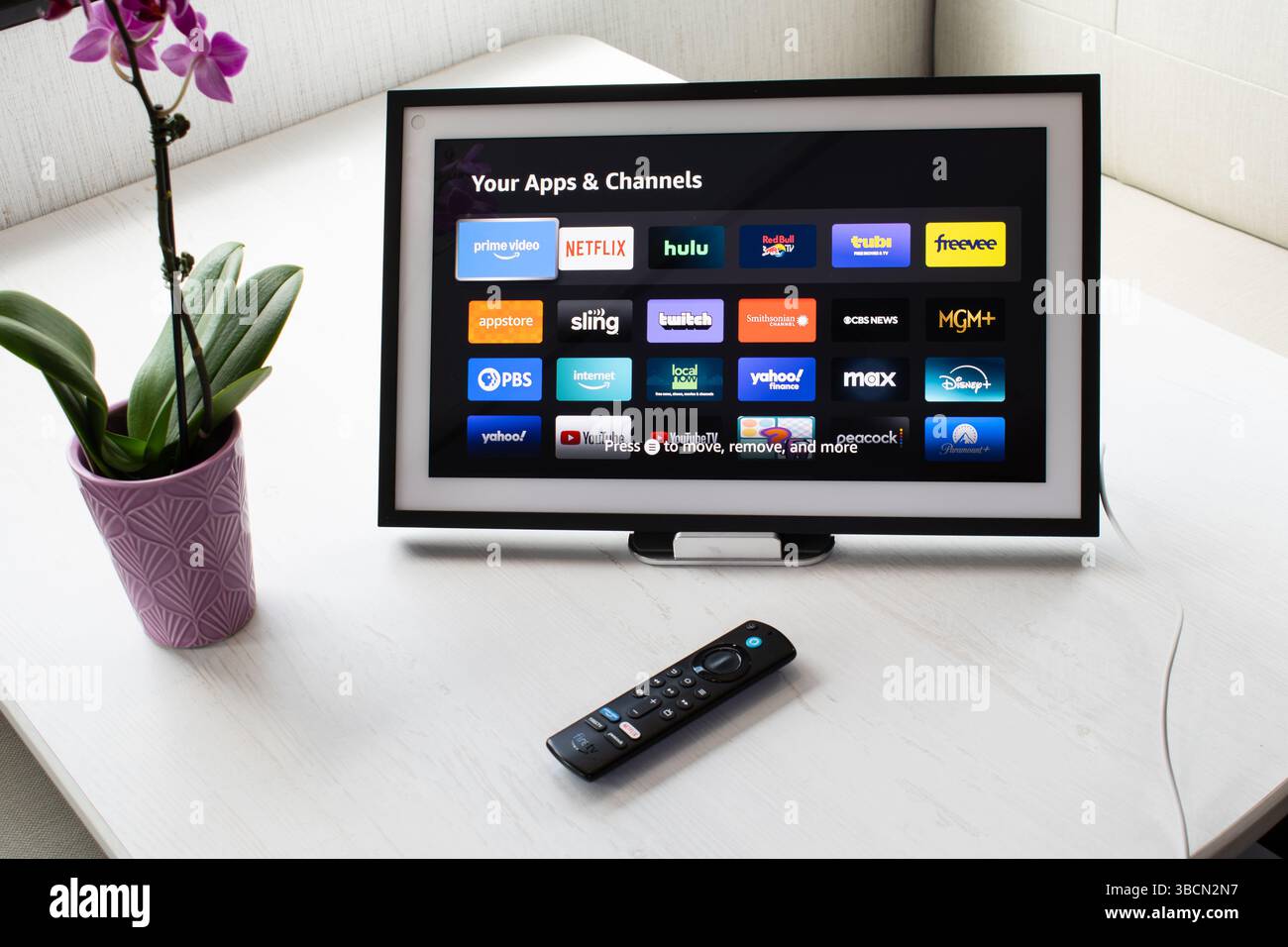 San Francisco, CA, 20 mai 2025 : Amazon Echo Show affiche des icônes d'application sur une table blanche avec télécommande Fire TV et orchidée dans une configuration de maison intelligente. Banque D'Images