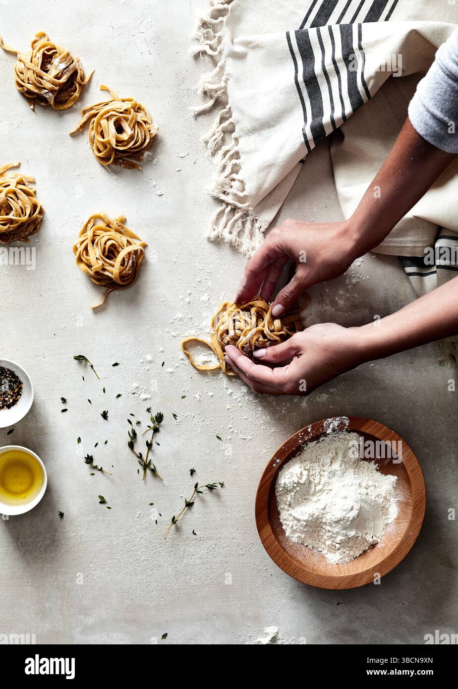 Mains façonnant des nids de pâtes fraîches sur une surface farinée avec des herbes Banque D'Images