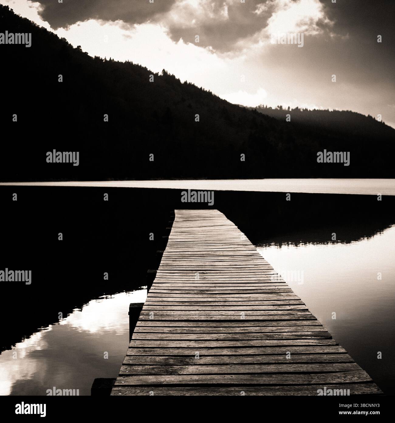 Une paisible jetée en bois s'étend sur les eaux calmes du lac Chambon, entourée de collines luxuriantes en Auvergne, en France. Banque D'Images