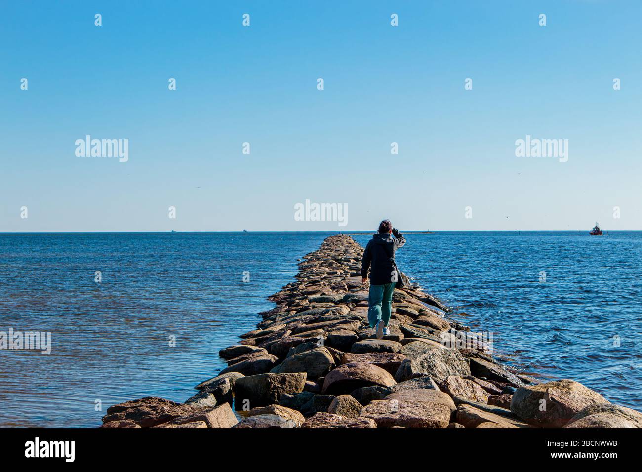 La femme marche sur la taupe de la rivière Pärnu en été. Jetée en pierre populaire dans la ville de Pärnu en Estonie. Banque D'Images