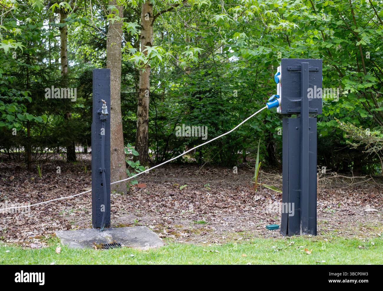 Un robinet d'eau et un point de branchement électrique dans un camping forestier Banque D'Images