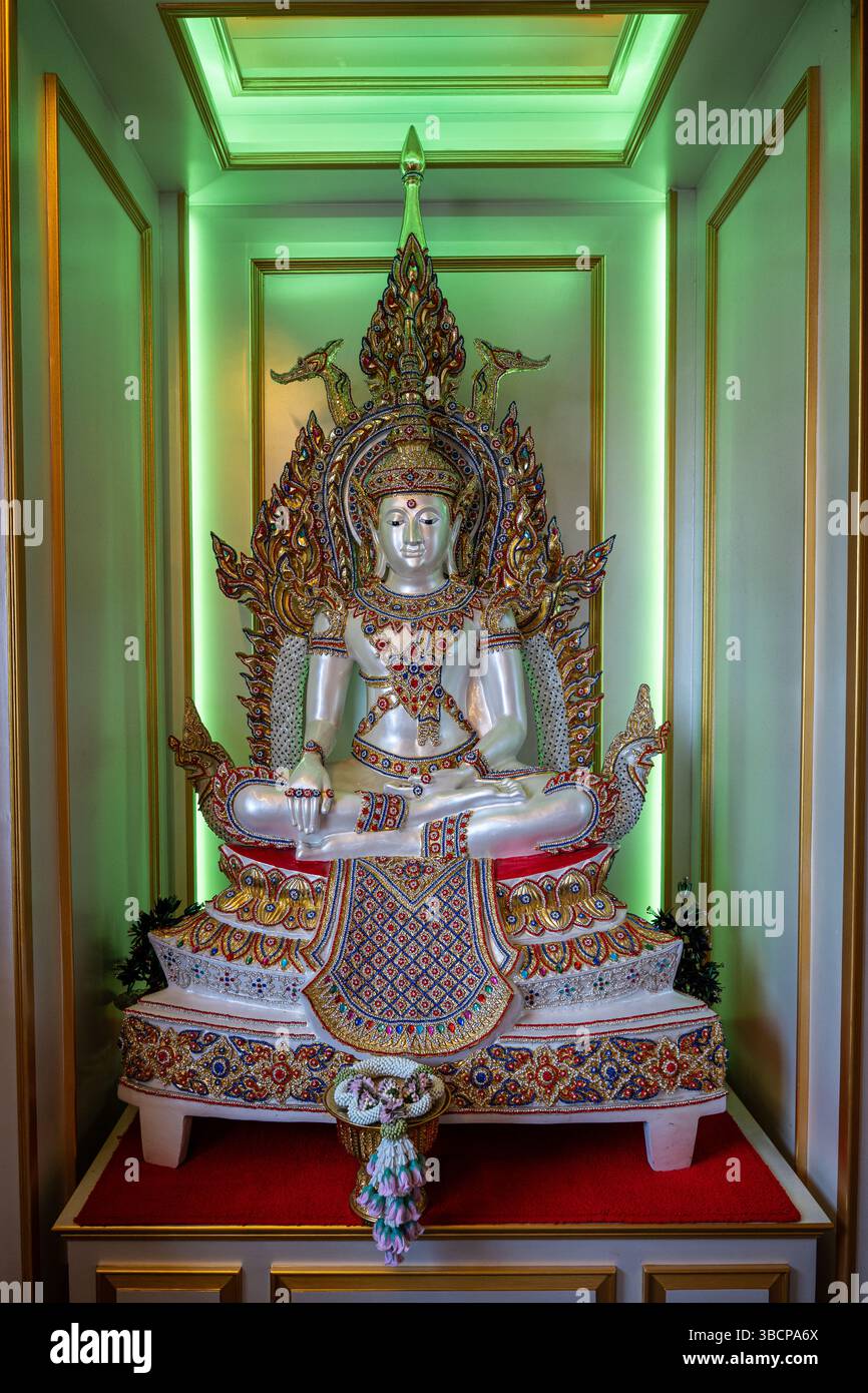 Statue de Bouddha en cristal blanc enchâssée dans une alcôve de temple thaïlandais. Une lumière verte douce rehausse son aura sereine et son artisanat thaïlandais traditionnel. Banque D'Images