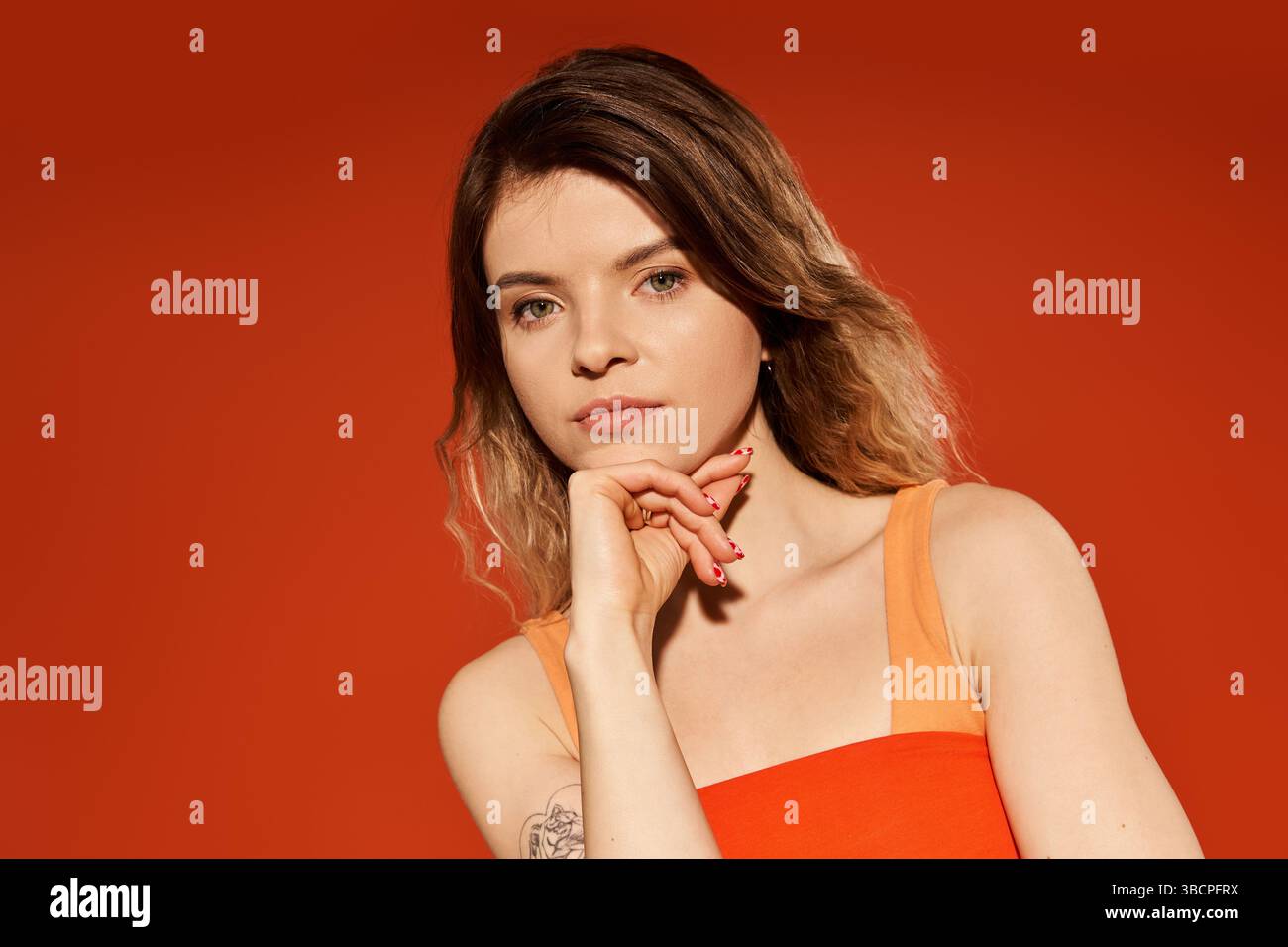 Une jeune femme élégante pose en toute confiance avec une expression réfléchie sur un fond orange. Banque D'Images