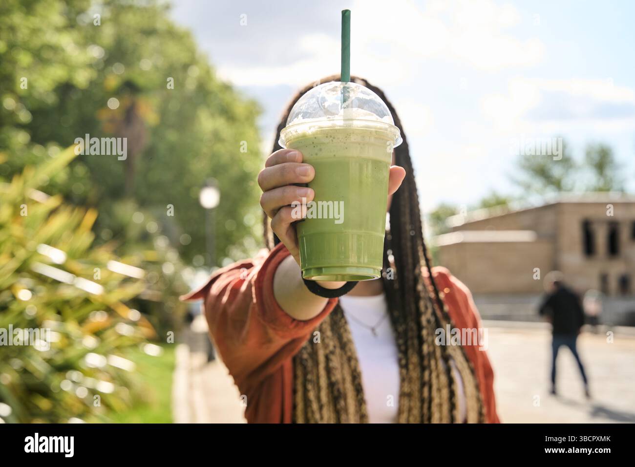 Touriste savourant un smoothie vert vibrant tout en profitant d'une journée d'été ensoleillée dans le parc, embrassant un style de vie rafraîchissant et sain Banque D'Images